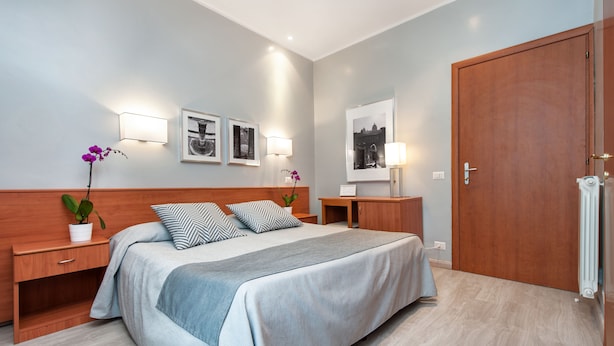 Une chambre à coucher moderne avec un grand lit, une tête de lit en bois, des tables de chevet et des lampes fixées au mur.