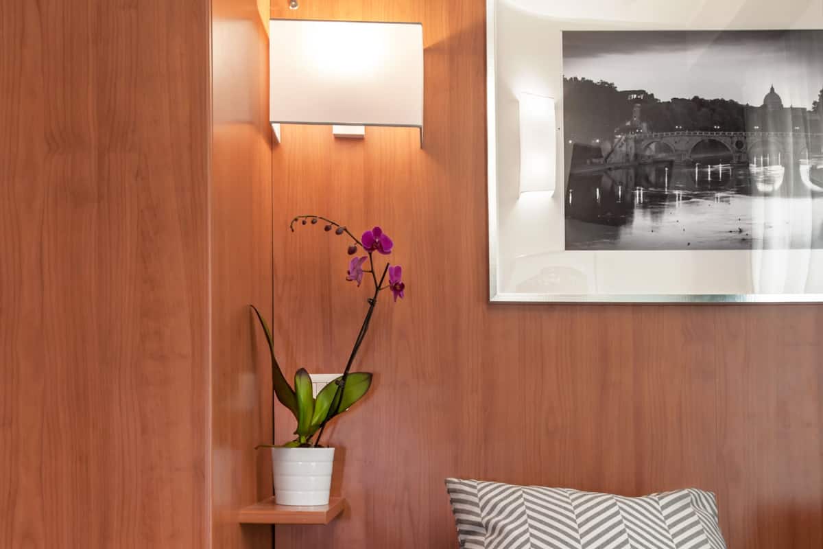 A bedroom with a bed, a nightstand, a wall-mounted shelf with a potted plant, and a framed picture on the wall.