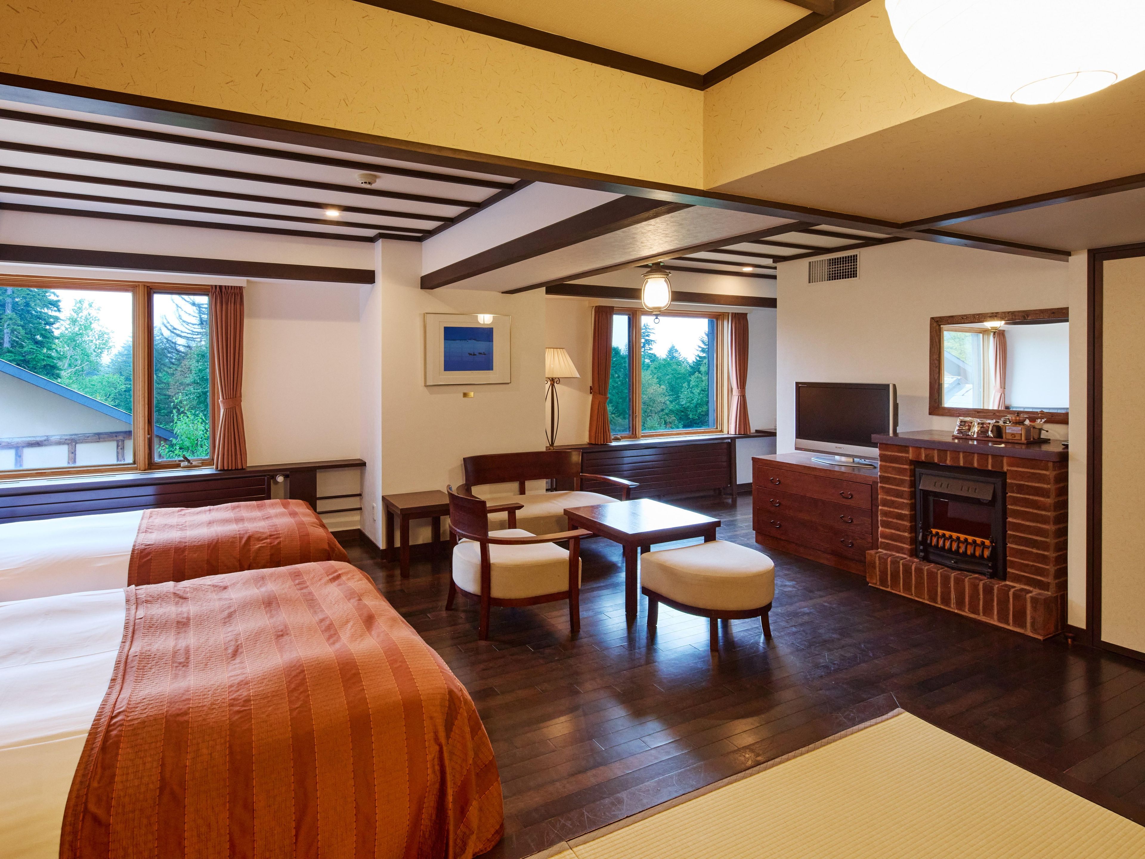 A hotel room with two beds, a desk, a chair, a television, a fireplace, and large windows with curtains.