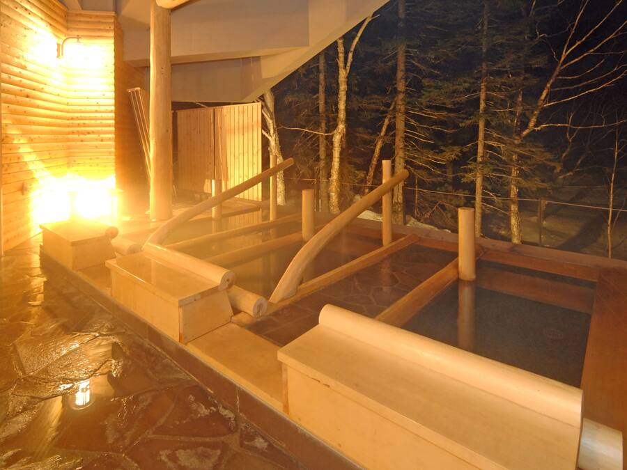 A hot spring bath area with wooden railings and a view of trees outside.