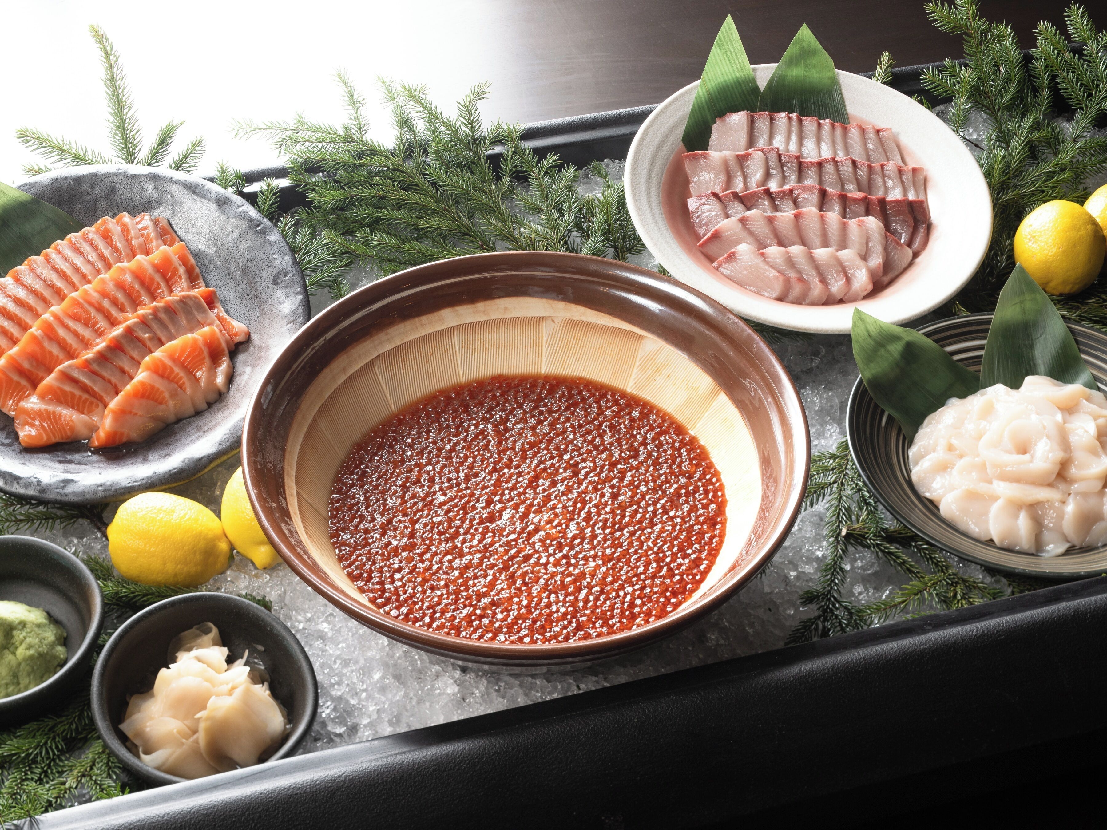 A tray with various seafood items, including sashimi, roe, and a bowl of red caviar.