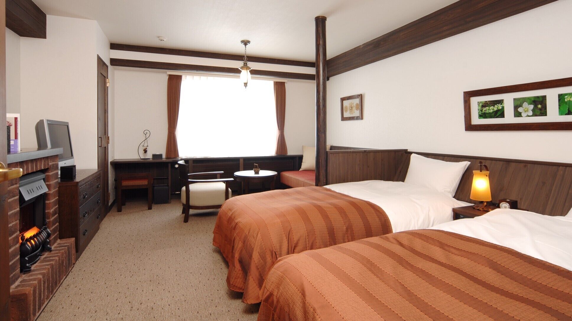 Een hotelkamer met twee bedden, een bureau, een stoel, een open haard en een raam met gordijnen.