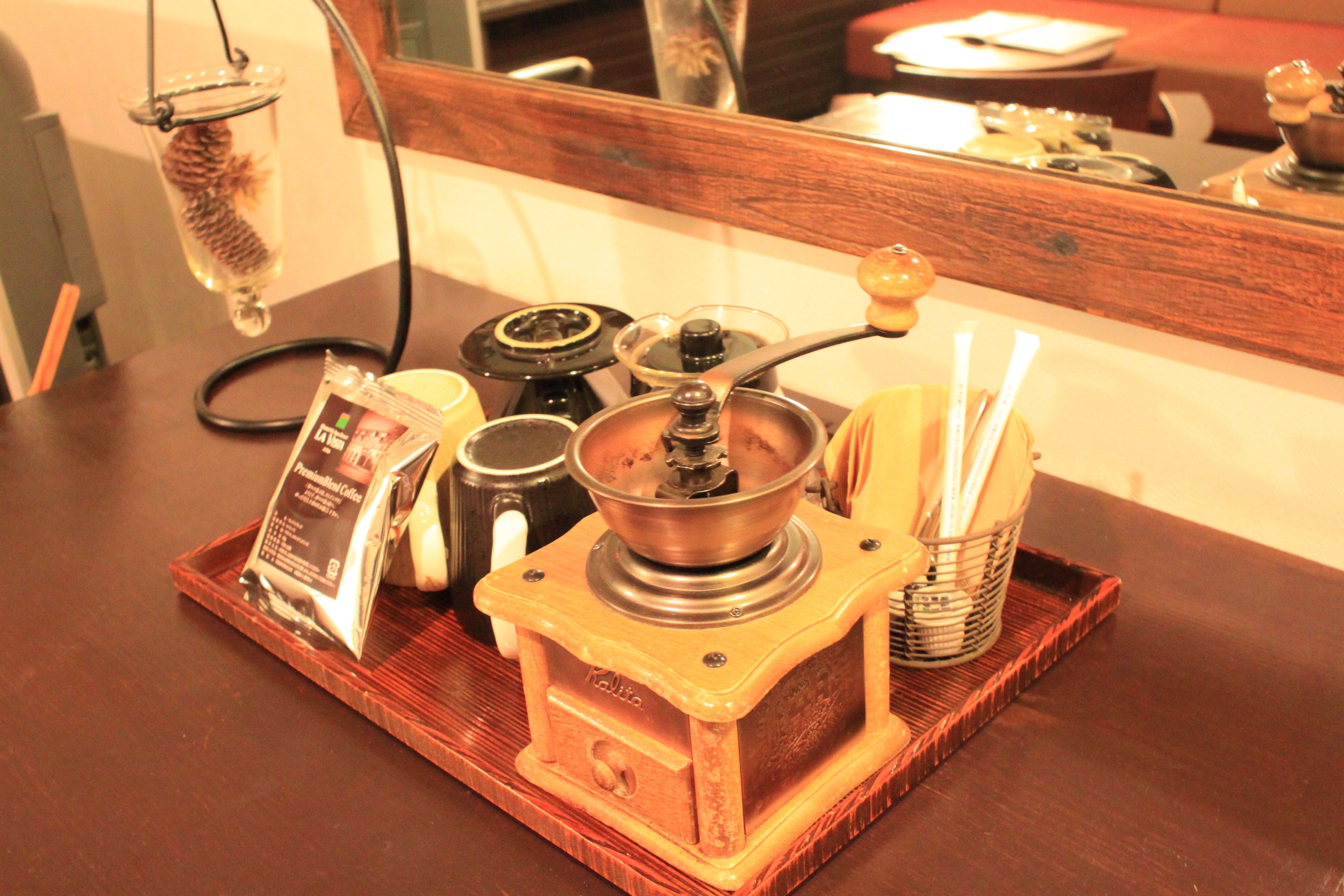 Eine Kaffeemühle auf einer Holztablett mit einer Kaffeepackung, einem Glasbehälter und einer Metalltasse.