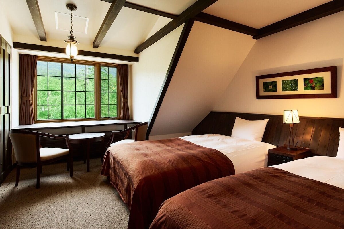 A hotel room with two beds, a desk, and a window with curtains.