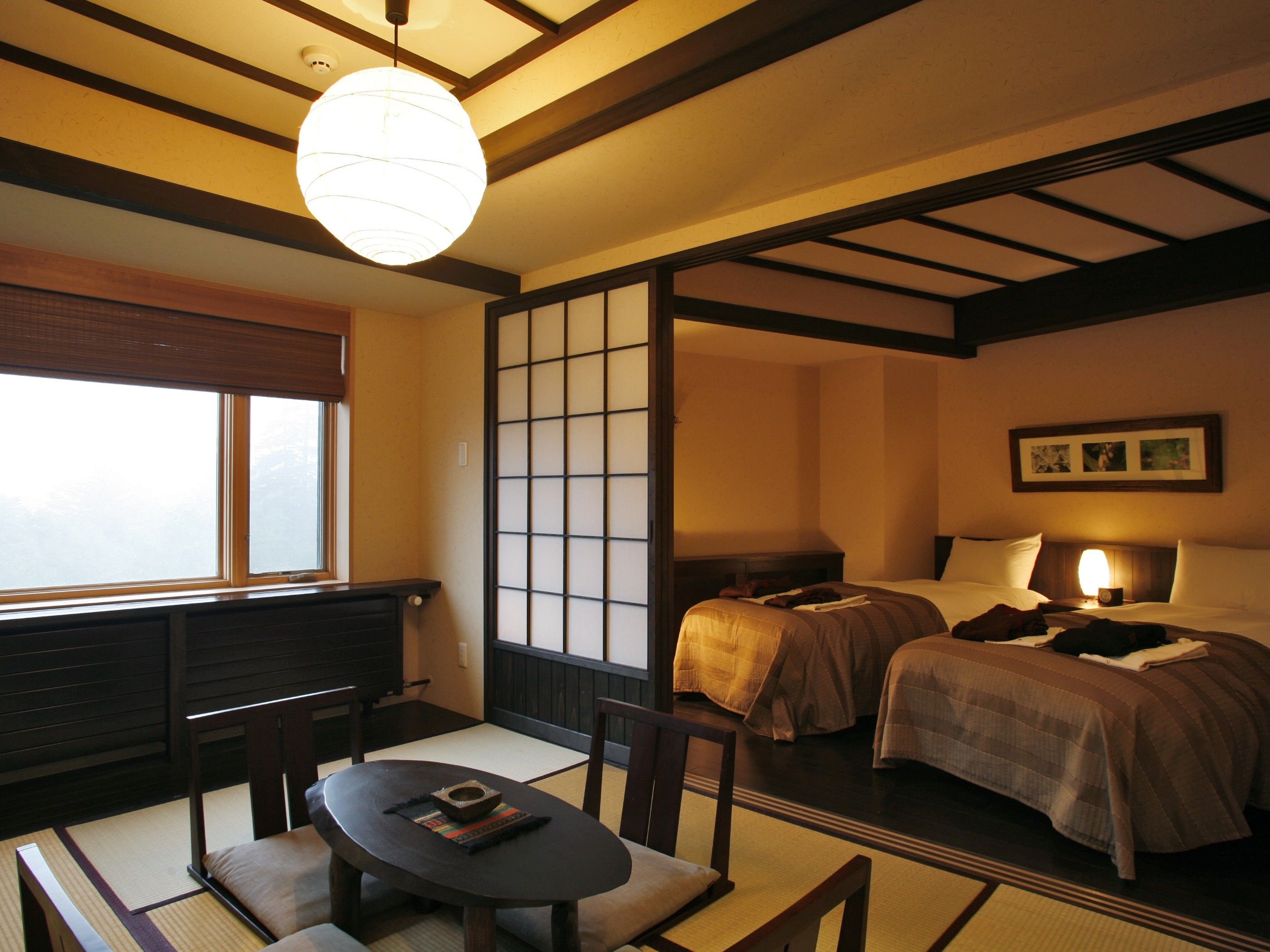 Una habitación de estilo japonés tradicional con suelo de tatami, una mesa baja con cojines, una cama con cabecera de madera y un celosía shoji.
