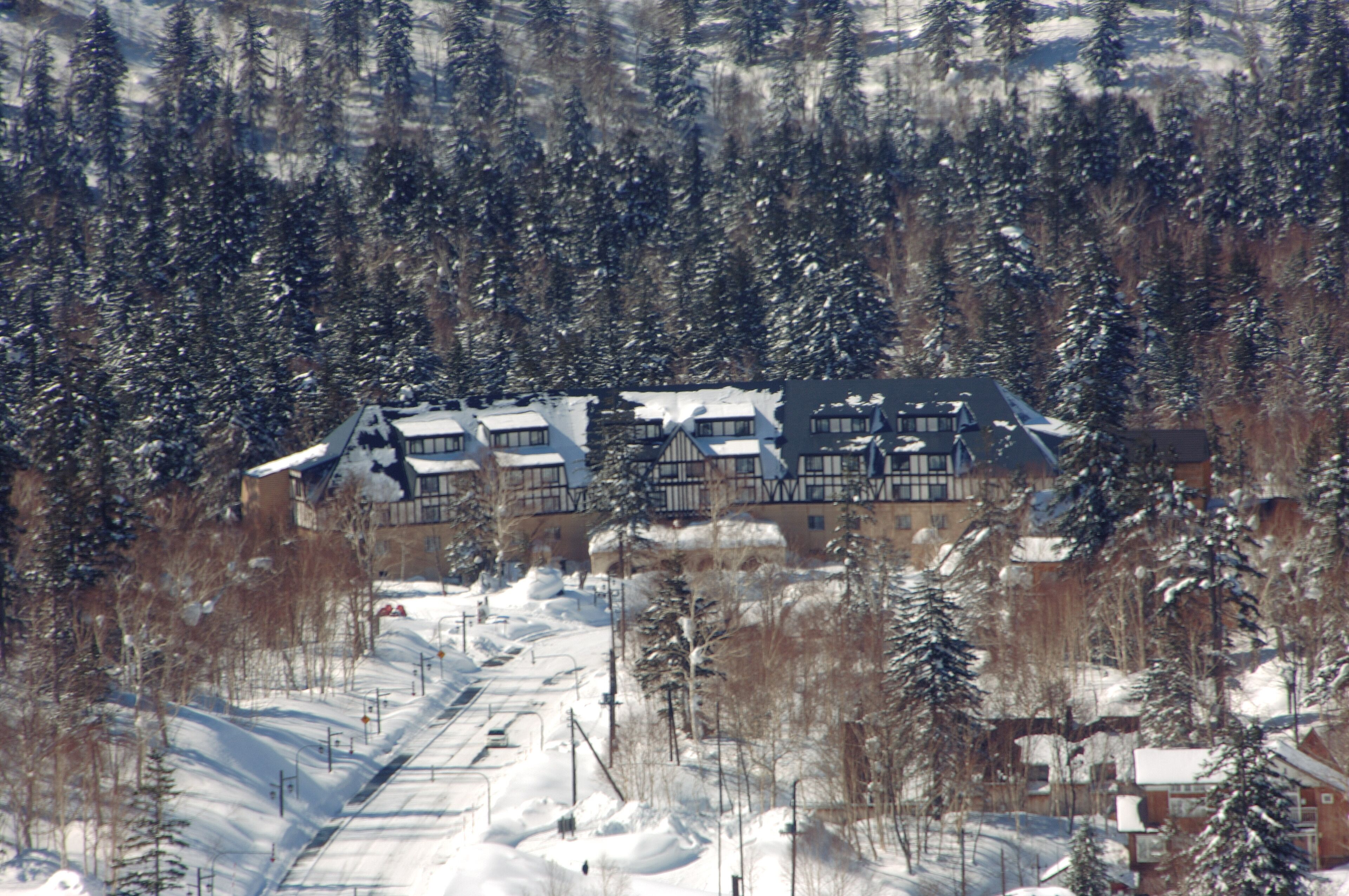 Un albergue cubierto de nieve con varias edificaciones, rodeado de árboles y una pista de esquí.