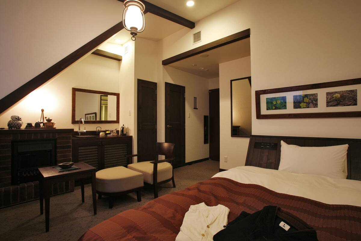 Une chambre d’hôtel avec un lit, un bureau, une chaise, une cheminée et un tableau encadré au mur.