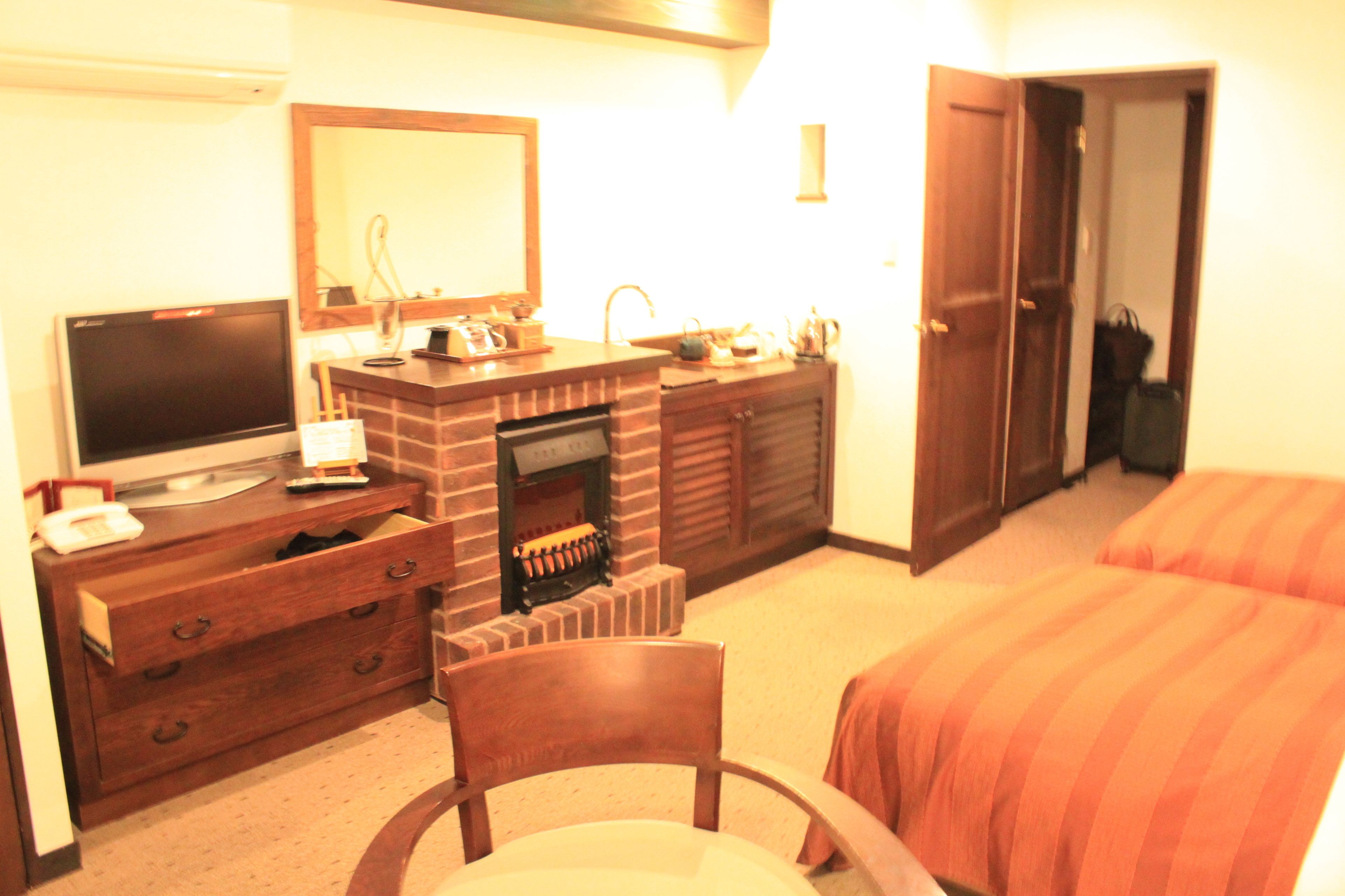 Una habitación de hotel con una cama, televisor, cómoda de madera, espejo y chimenea.