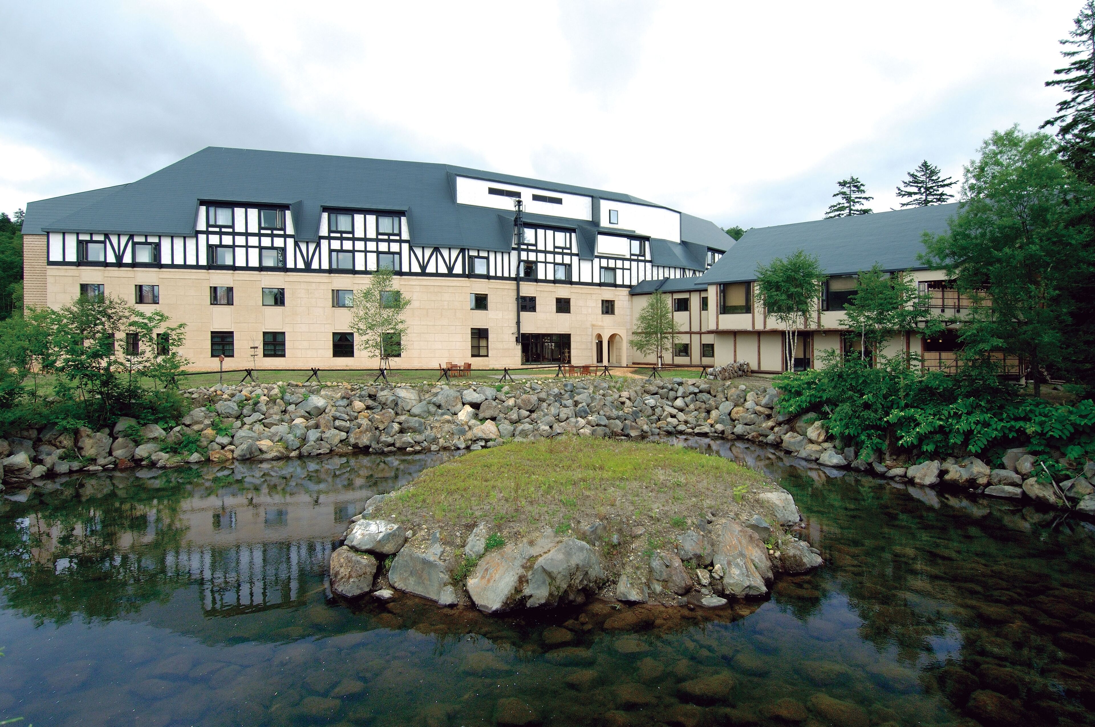 A modern building with a stone facade and a large pond in front.