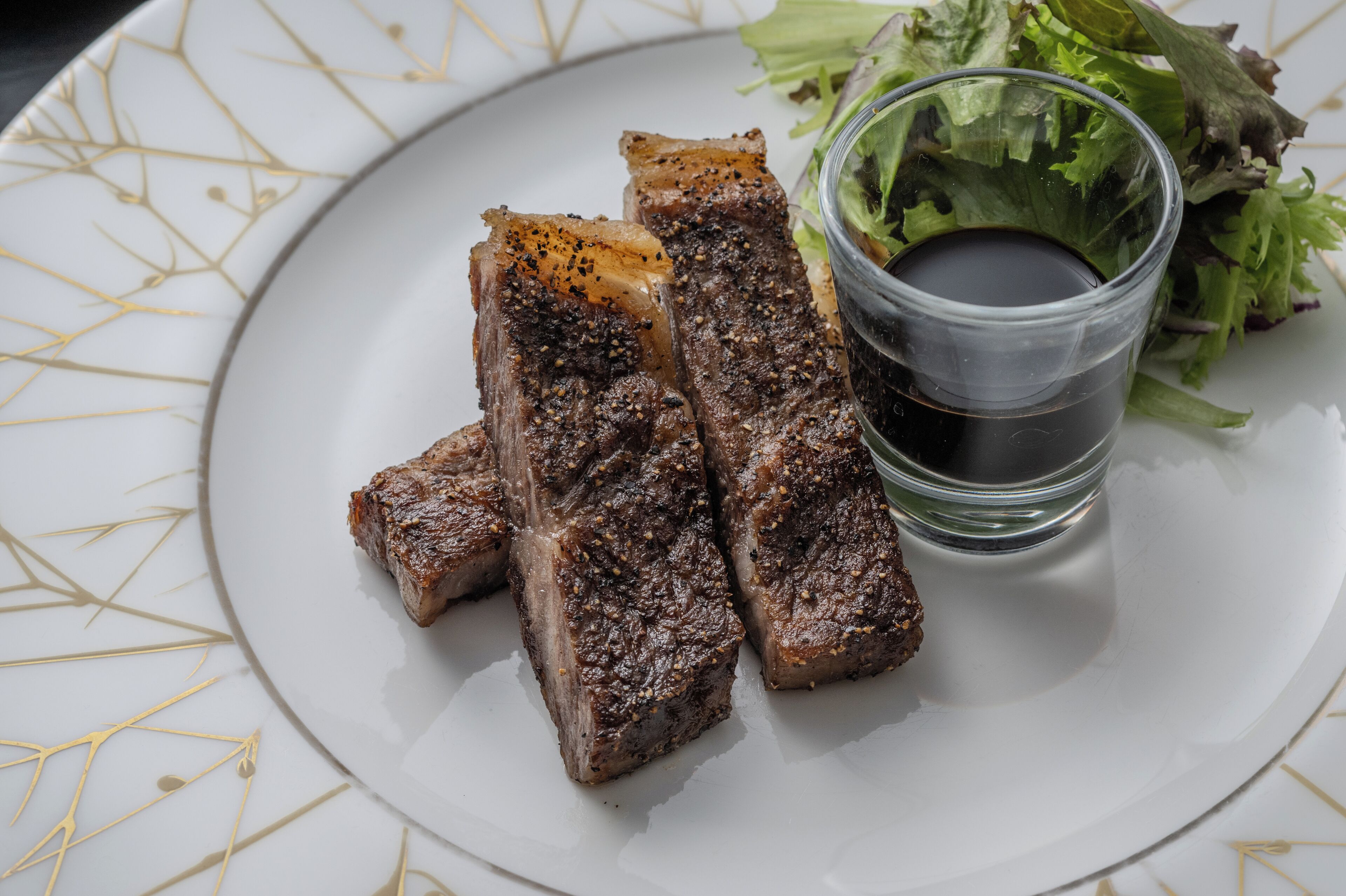 Une assiette de viande grillée, un ramequin de sauce et une salade en accompagnement.