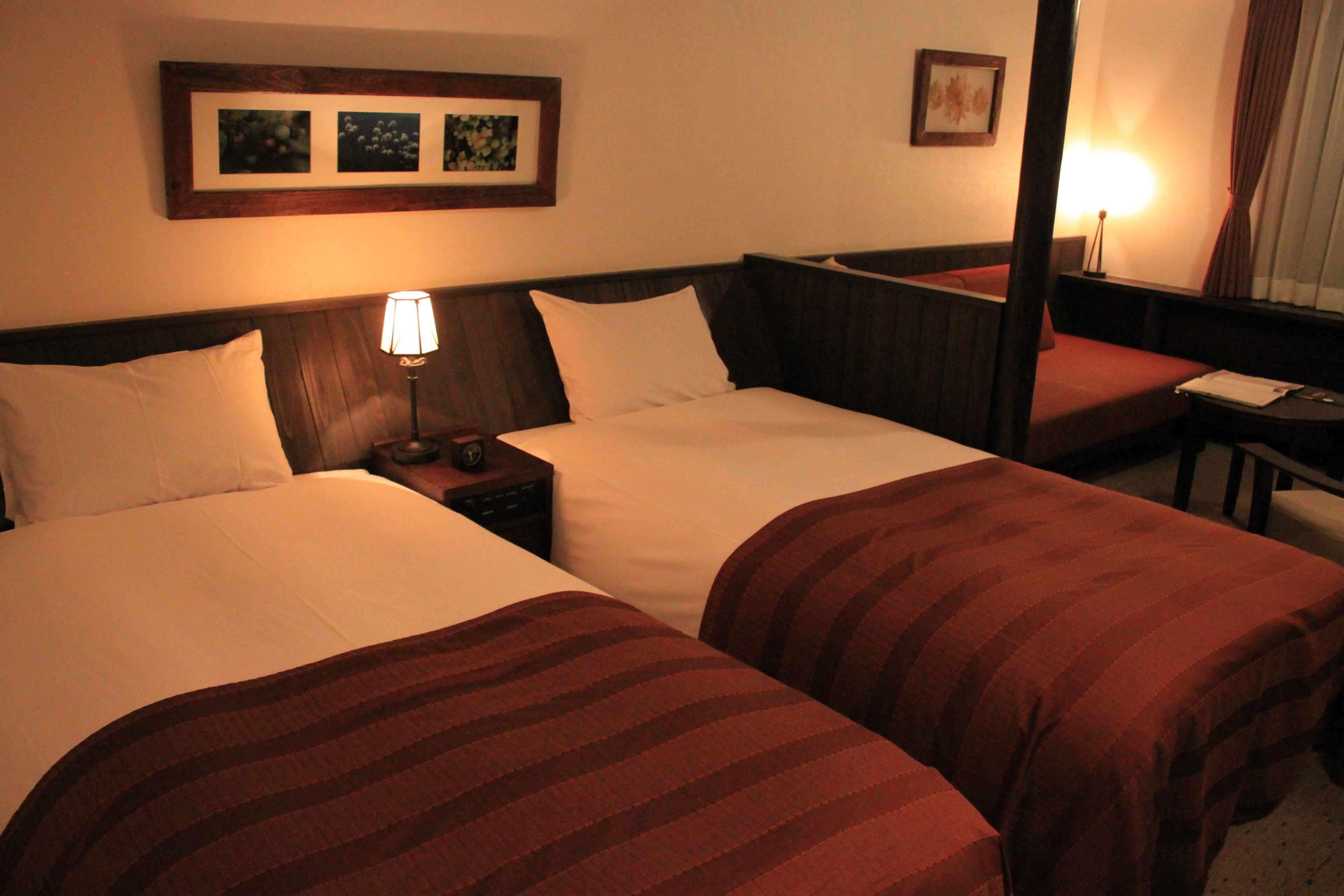 A hotel room with two beds, a nightstand, a lamp, and framed pictures on the wall.