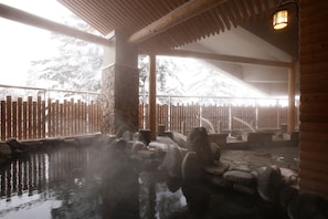 A traditional Japanese onsen with stone hot spring baths, wooden railings, and a stone wall backdrop. - La Vista Daisetsuzan (Higashikawa)