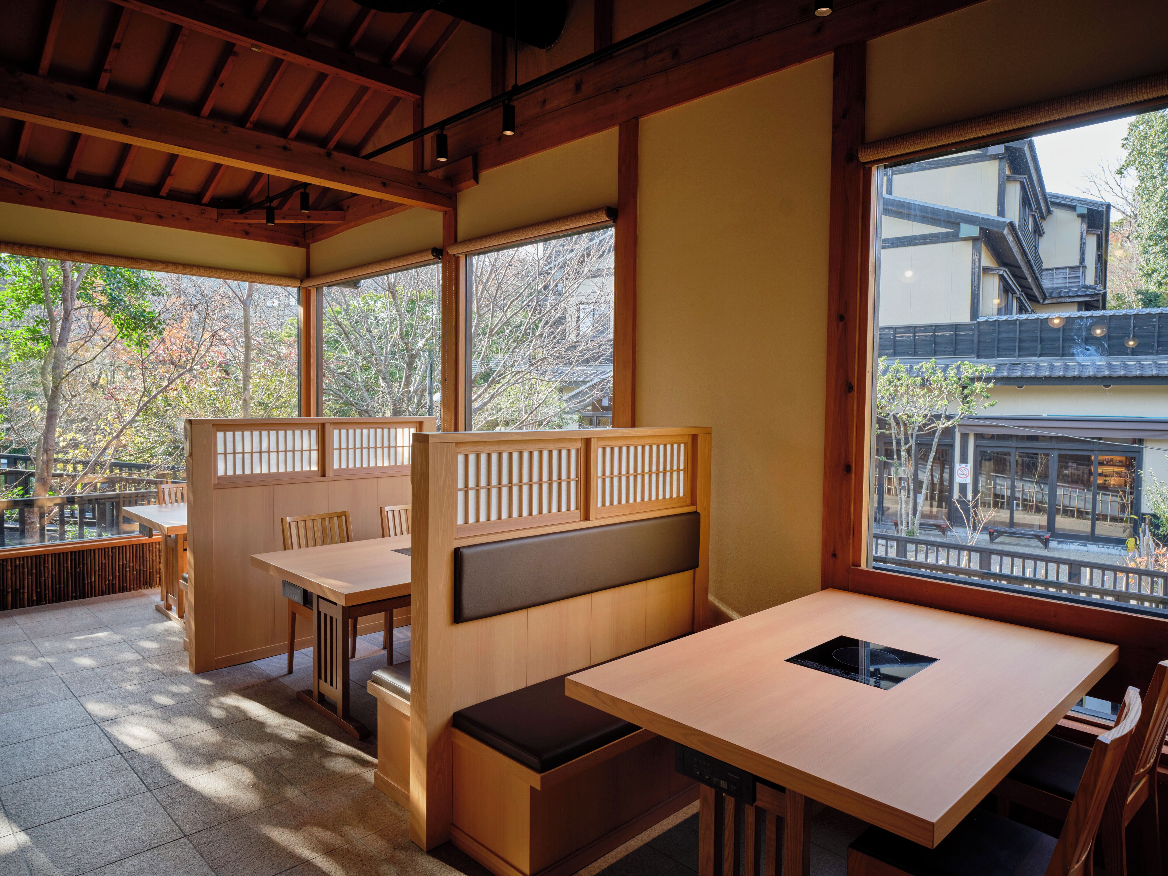 A traditional Japanese restaurant interior with tatami mat flooring, wooden furniture, and large windows offering a view of the outside.