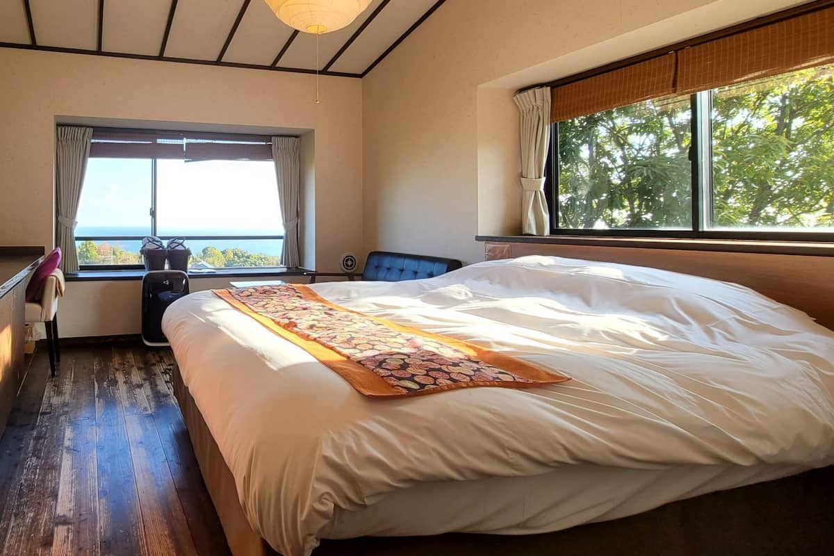A hotel room with a bed, a desk with a computer, a window with a view, and a ceiling fan.