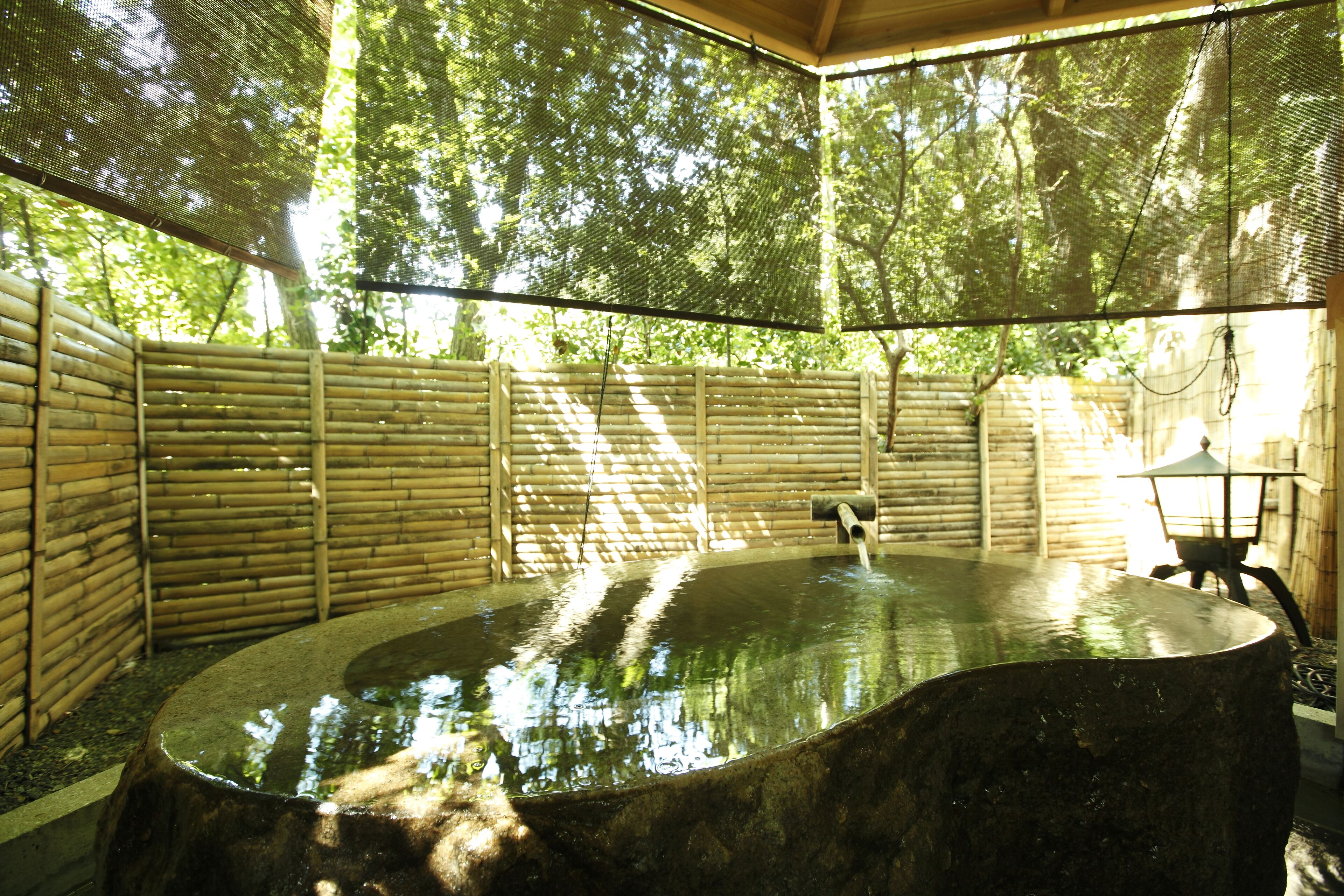 A hot spring area with a stone basin, bamboo walls, and a lantern.