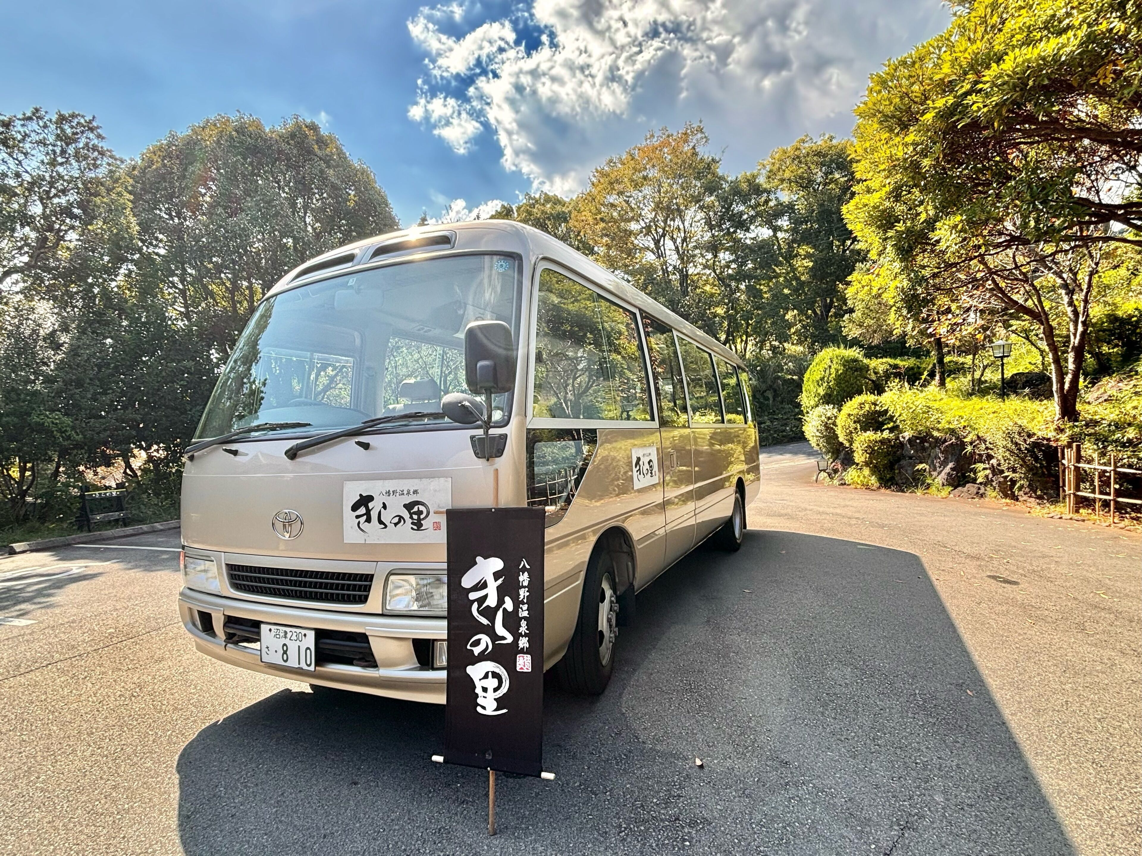A beige minibus parked on a road with a signboard in front.