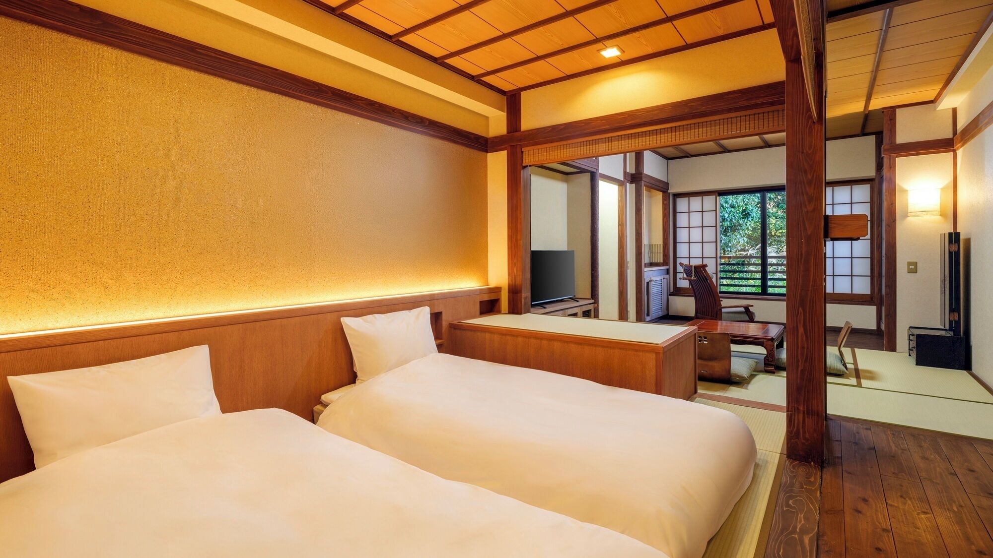 Hotellihuone, jossa on kaksi sänkyä, televisio ja perinteinen japanilaistyylinen sisustus.