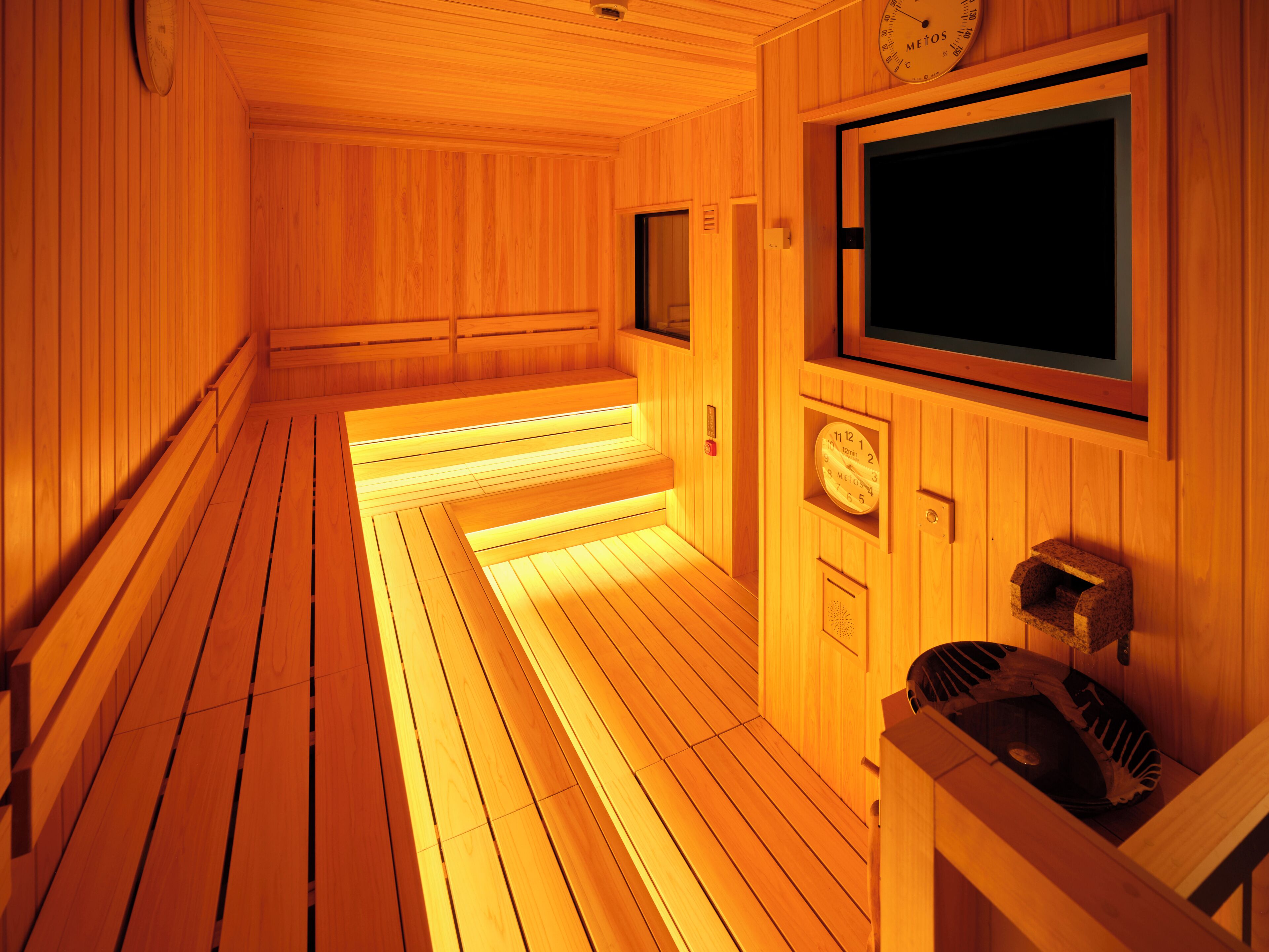 A sauna room with wooden walls and benches, a clock, and a television.