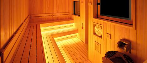 A sauna room with wooden walls and benches, a clock, and a television.