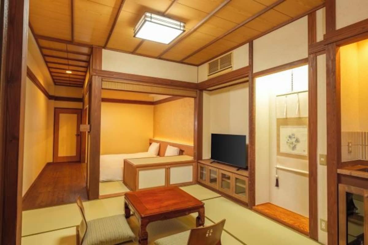 Une pièce de style japonais traditionnel, avec un sol recouvert de tatamis, une basse table en bois, un canapé et un téléviseur.