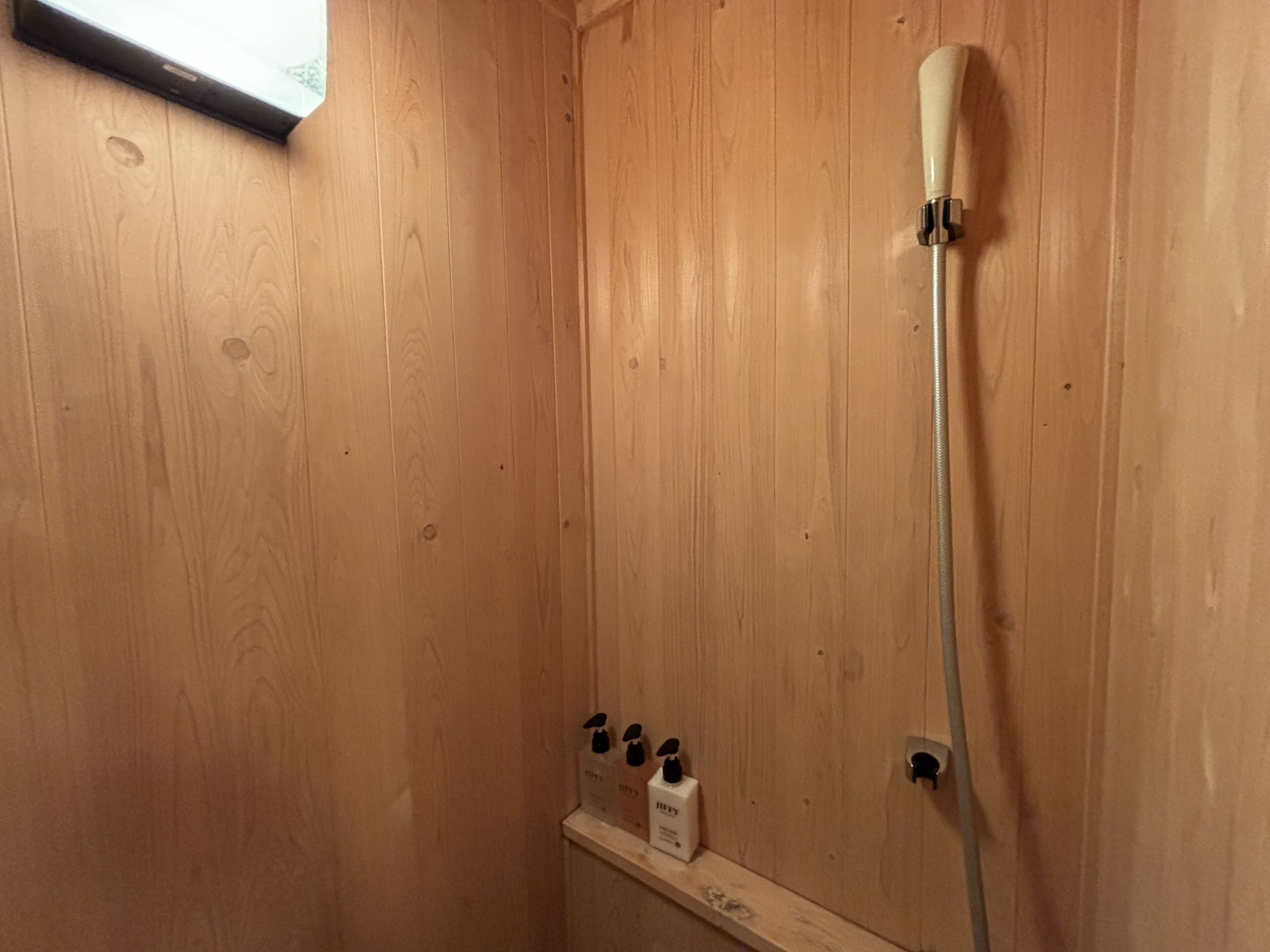 Eine Duschrückwand aus Holz mit Duschbrauseisen und einer Seifenspenderhalterung an der Wand.