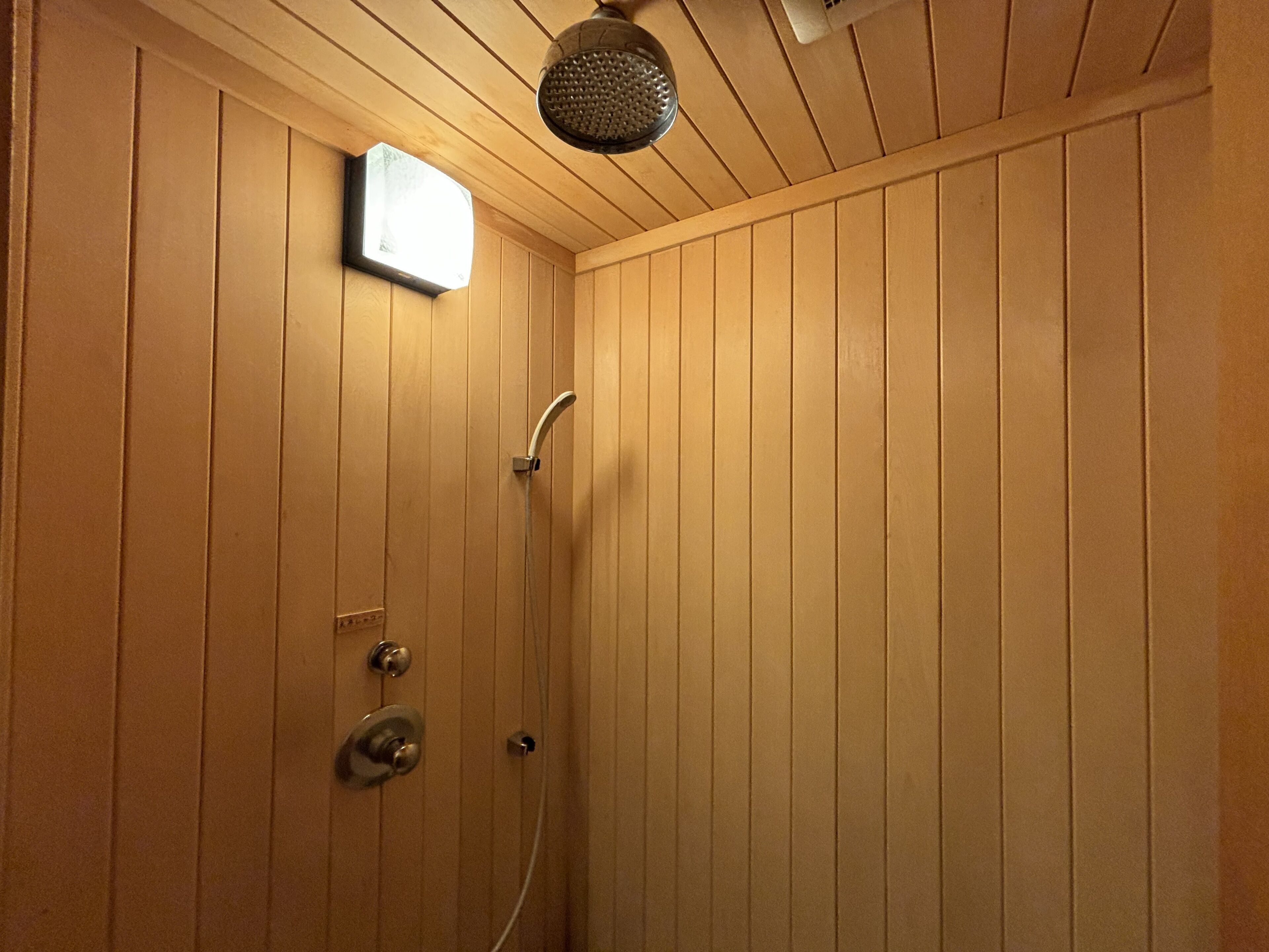 A wooden-paneled shower room with a handheld showerhead and a wall-mounted control panel.