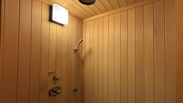 Un baño con paneles de madera, cabezal de ducha de mano y panel de control en la pared.