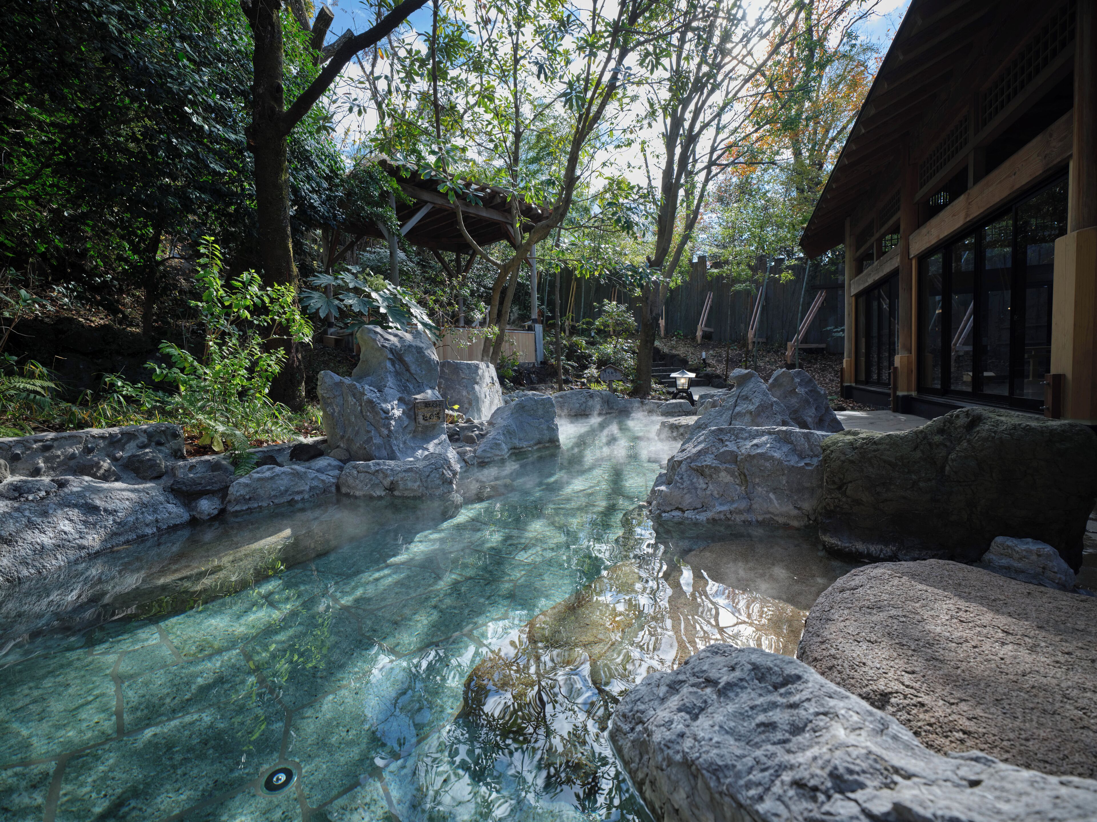 Ein traditionelles japanisches Onsen mit klarem Thermalwasser, umgeben von Felsen und Bäumen.