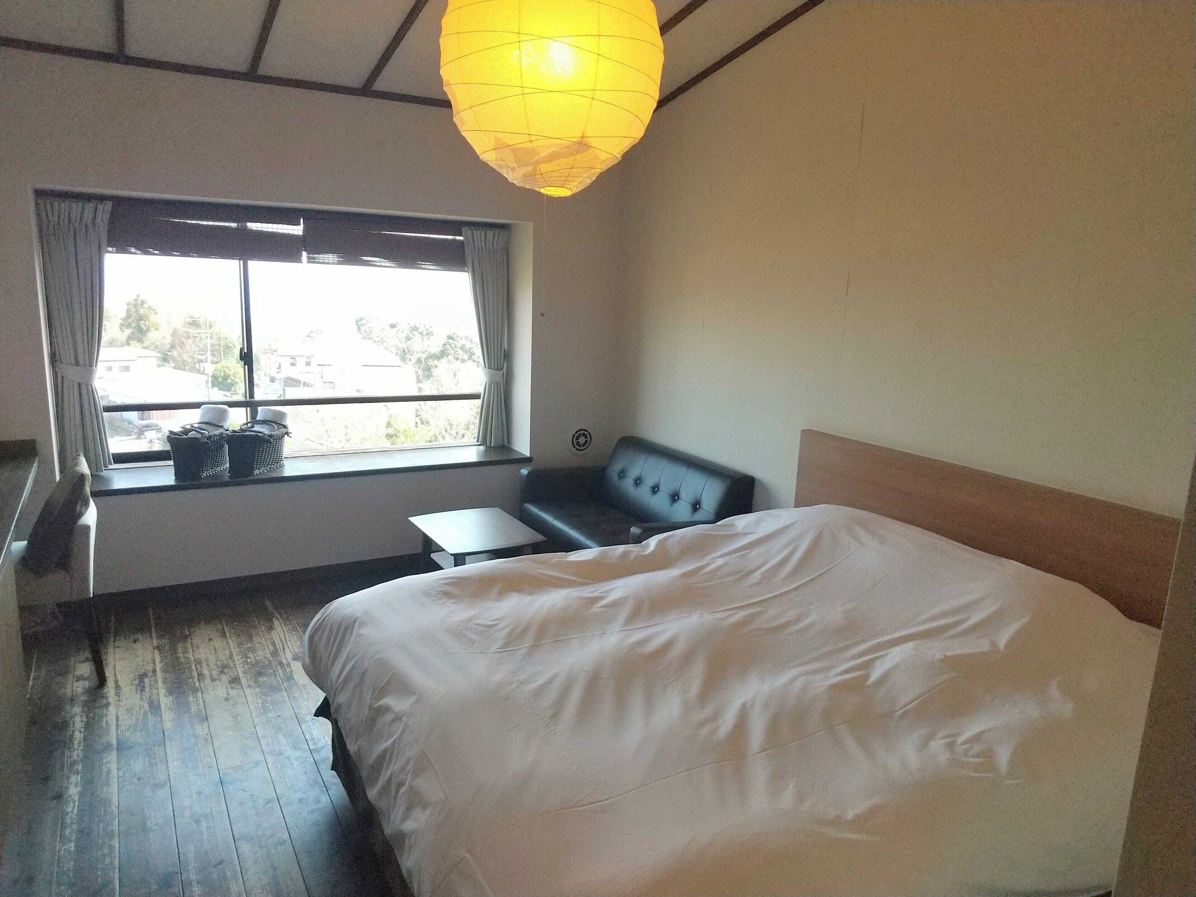 A hotel room with a large bed, a small table, a sofa, and a window with curtains.
