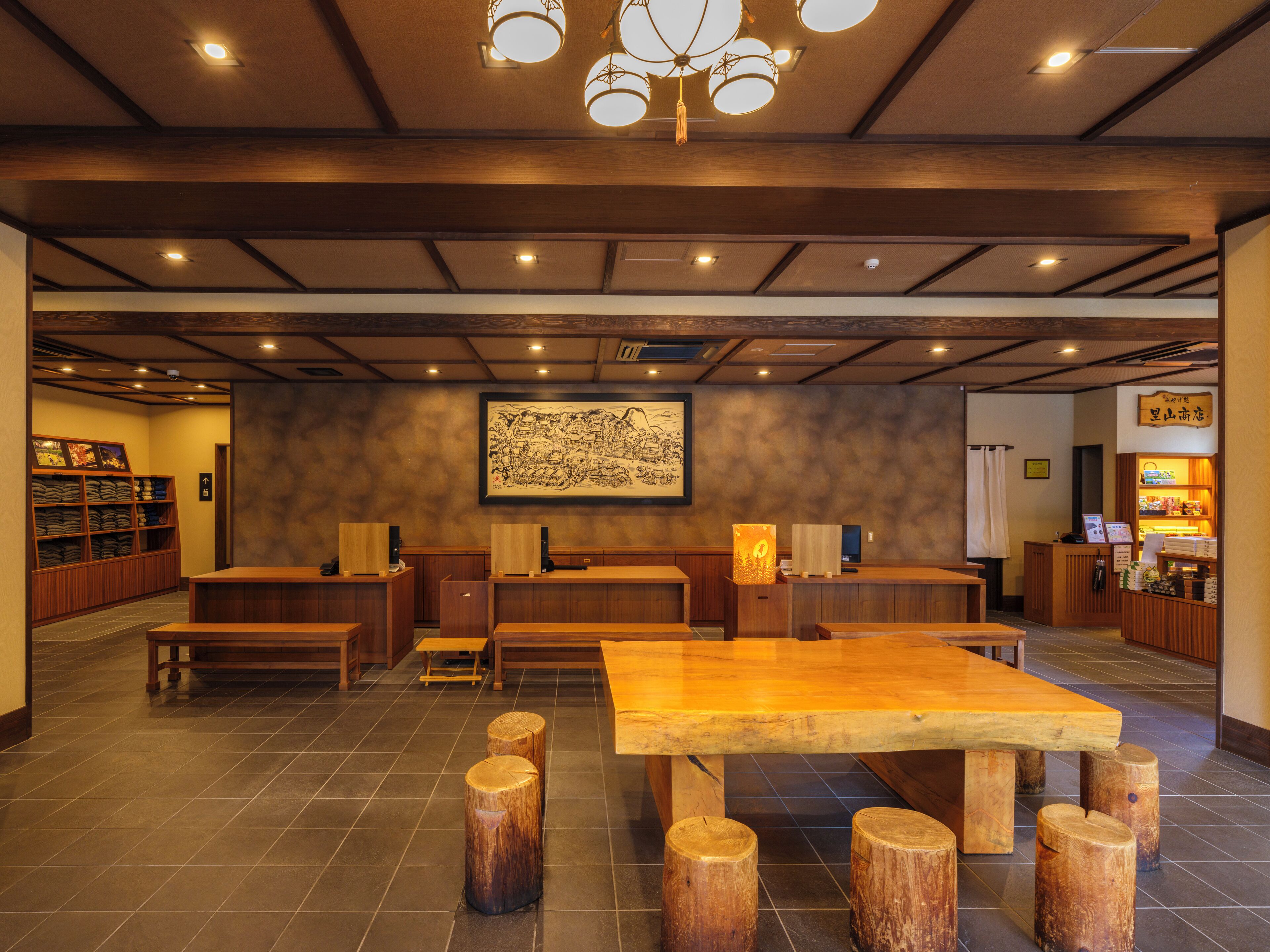 A spacious lobby with wooden benches and tables, a large framed artwork on the wall, and a reception desk with a sign.