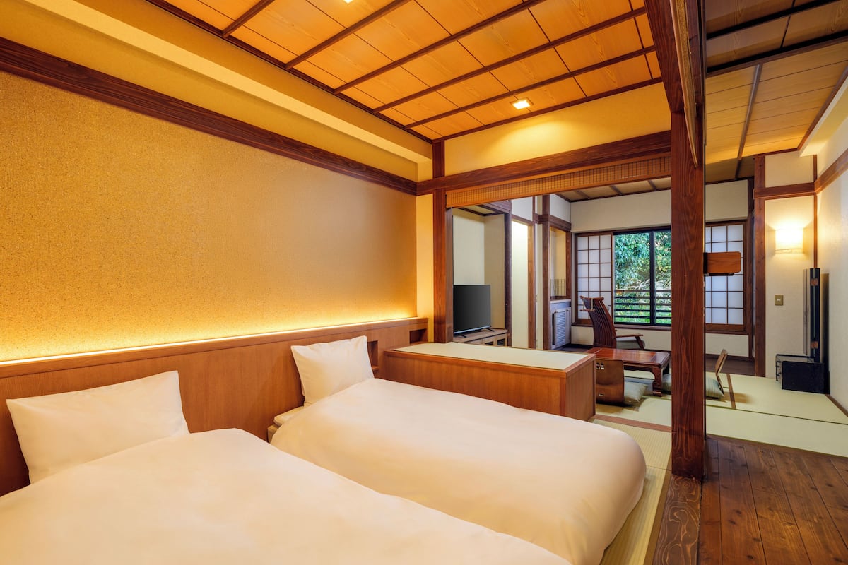 A traditional Japanese-style room with two beds, a television, and a view of a garden through a sliding door.