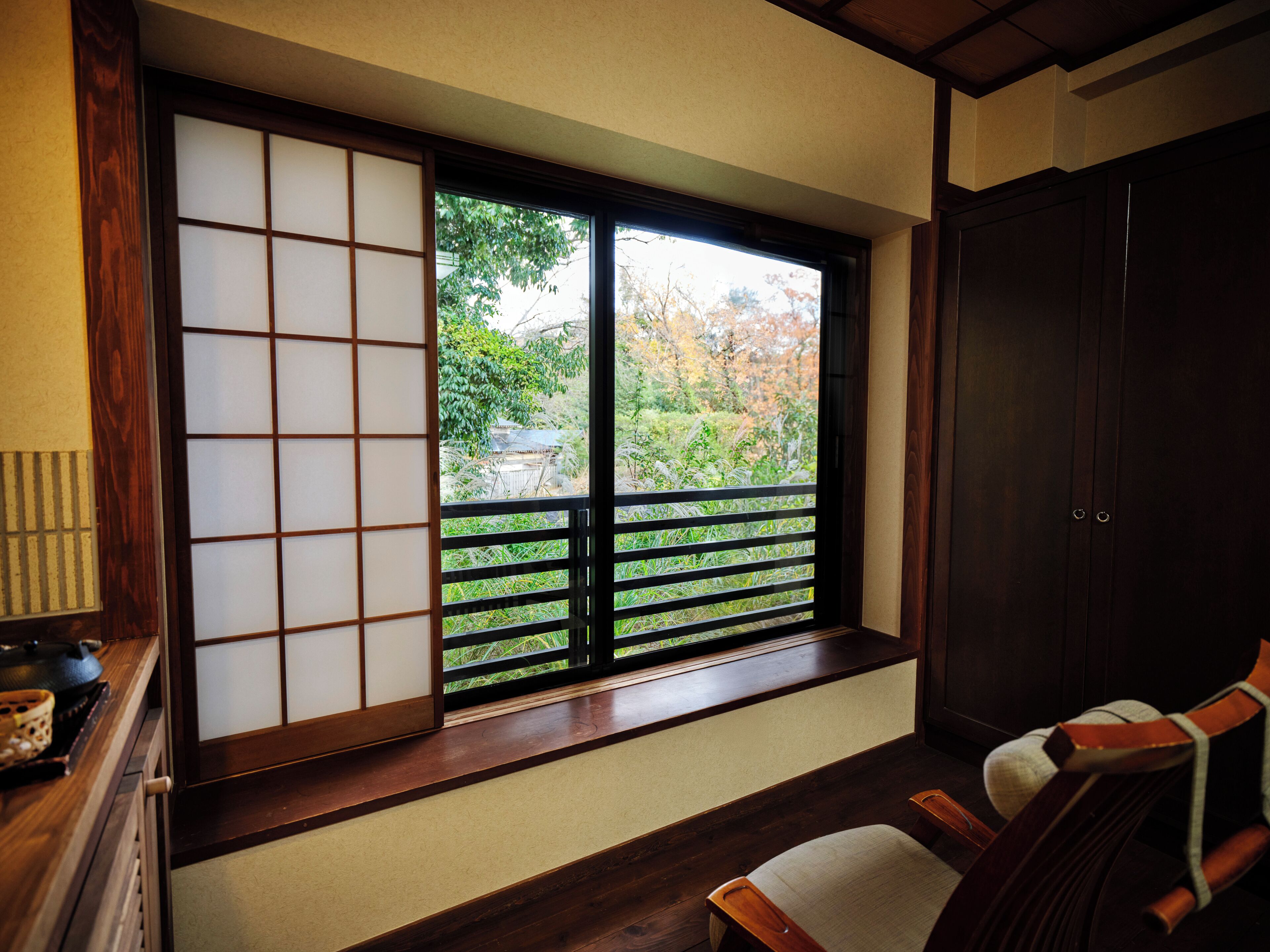 A traditional Japanese room with tatami flooring, a sliding shoji screen, a dark wooden wardrobe, and a view of a garden.