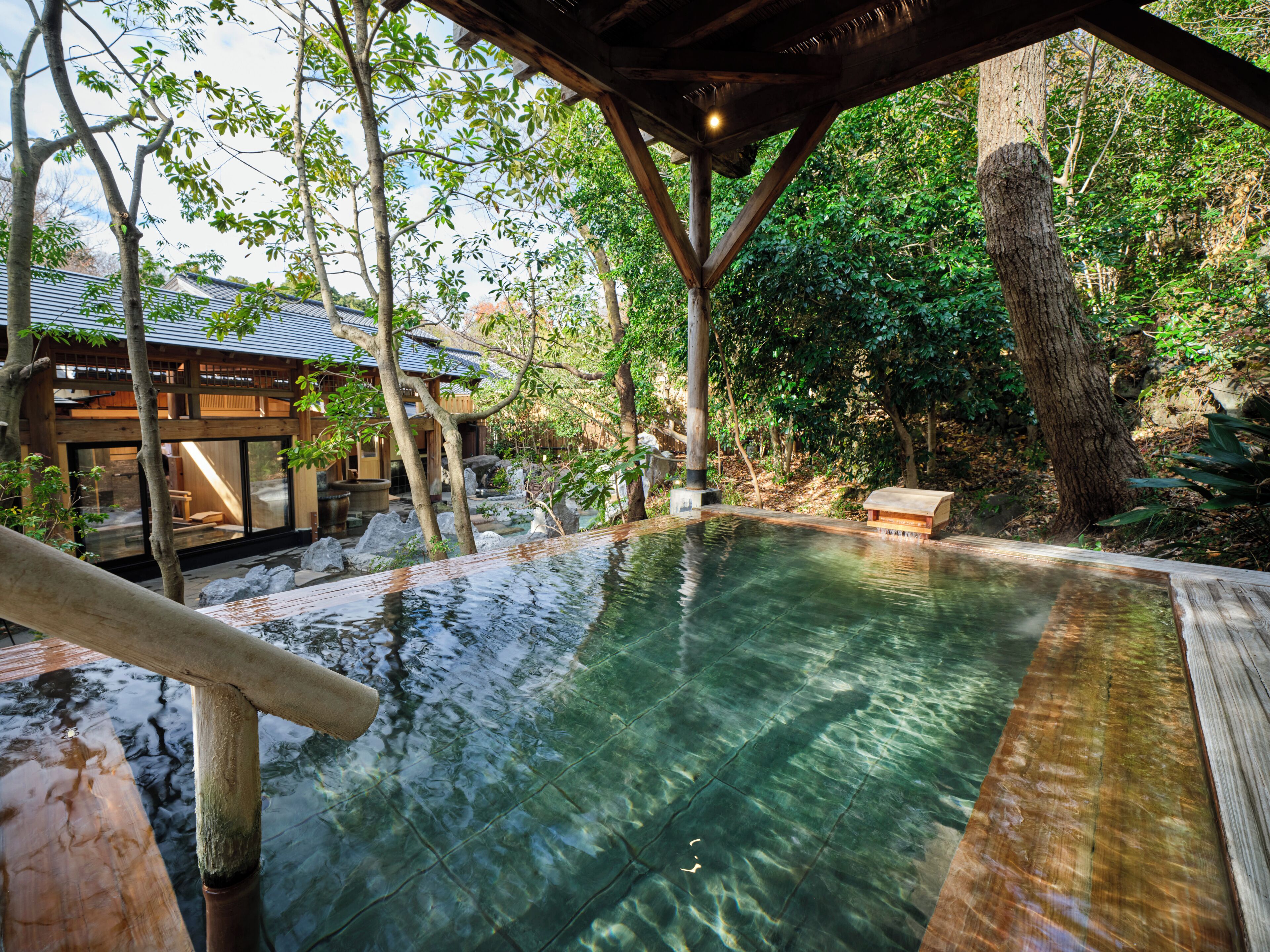 Un onsen japonés tradicional rodeado de paisajes naturales, estructuras de madera y una terraza de madera.