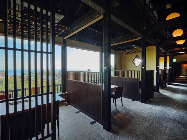 Ein Restaurant mit Meerblick, Holzmöbeln und einer hohen Decke mit freiliegenden Balken.
