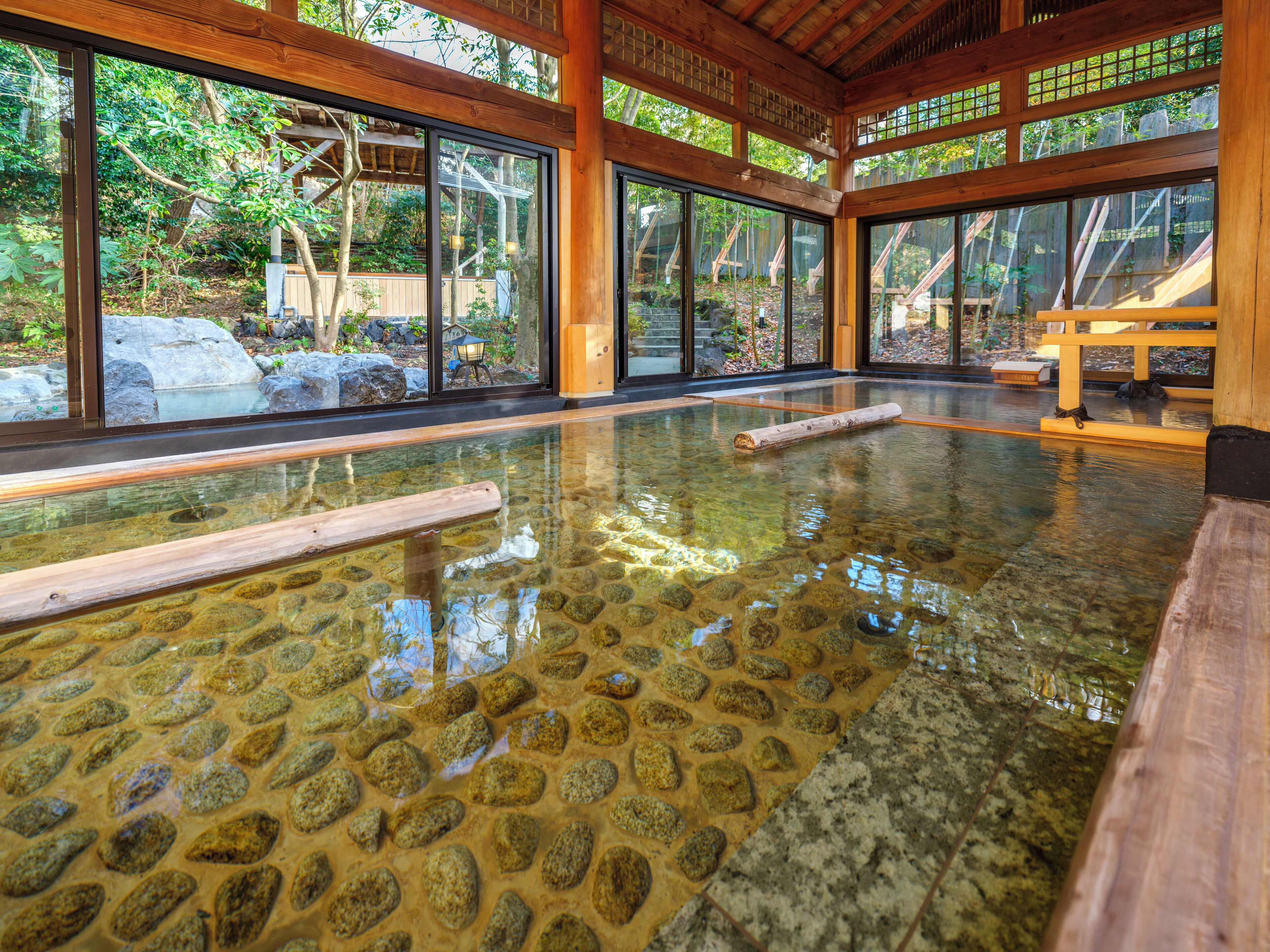 A traditional Japanese onsen with a stone bath, wooden beams, and large windows.