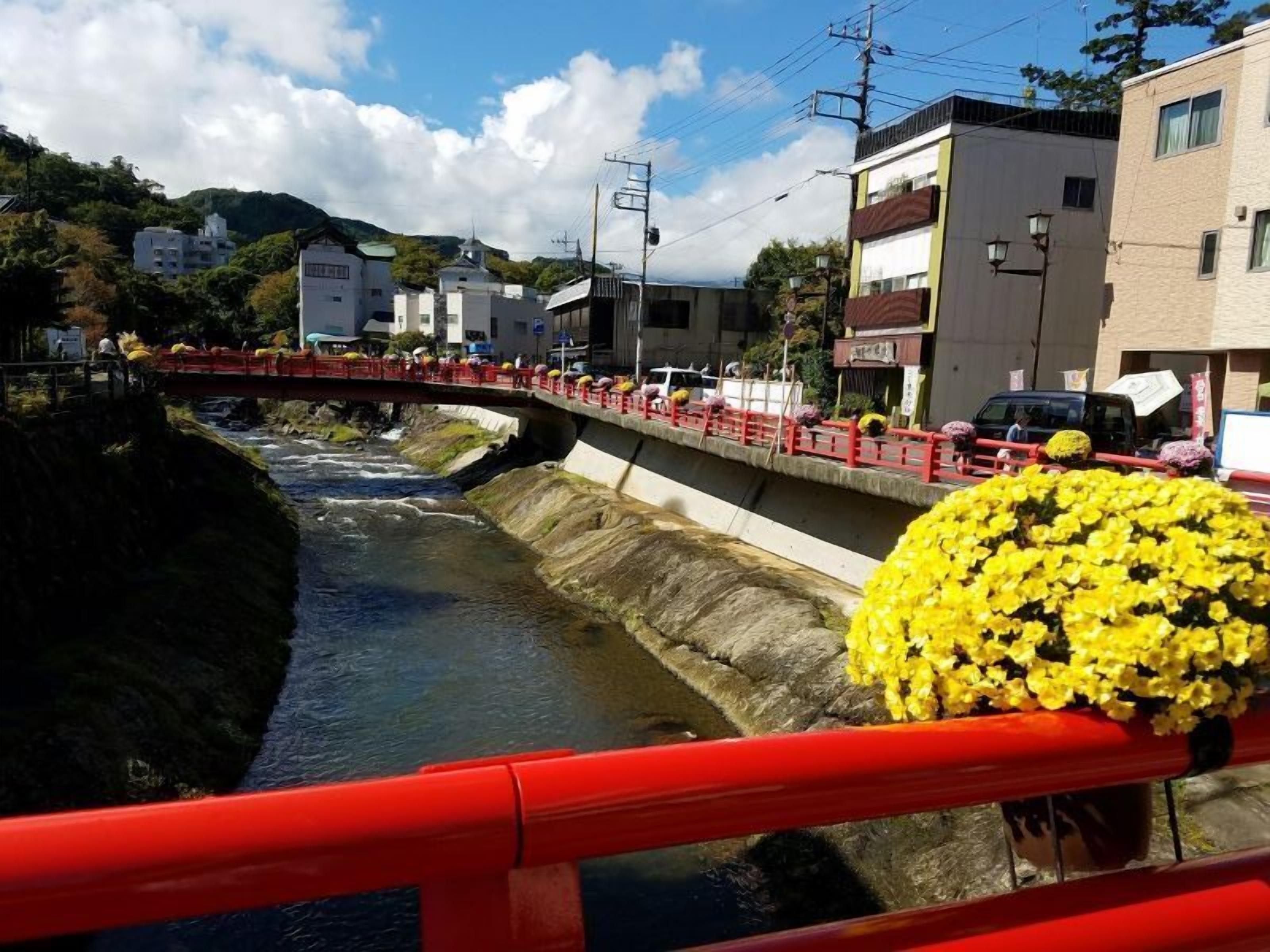 A river with a concrete embankment, a red bridge, and buildings in the background.