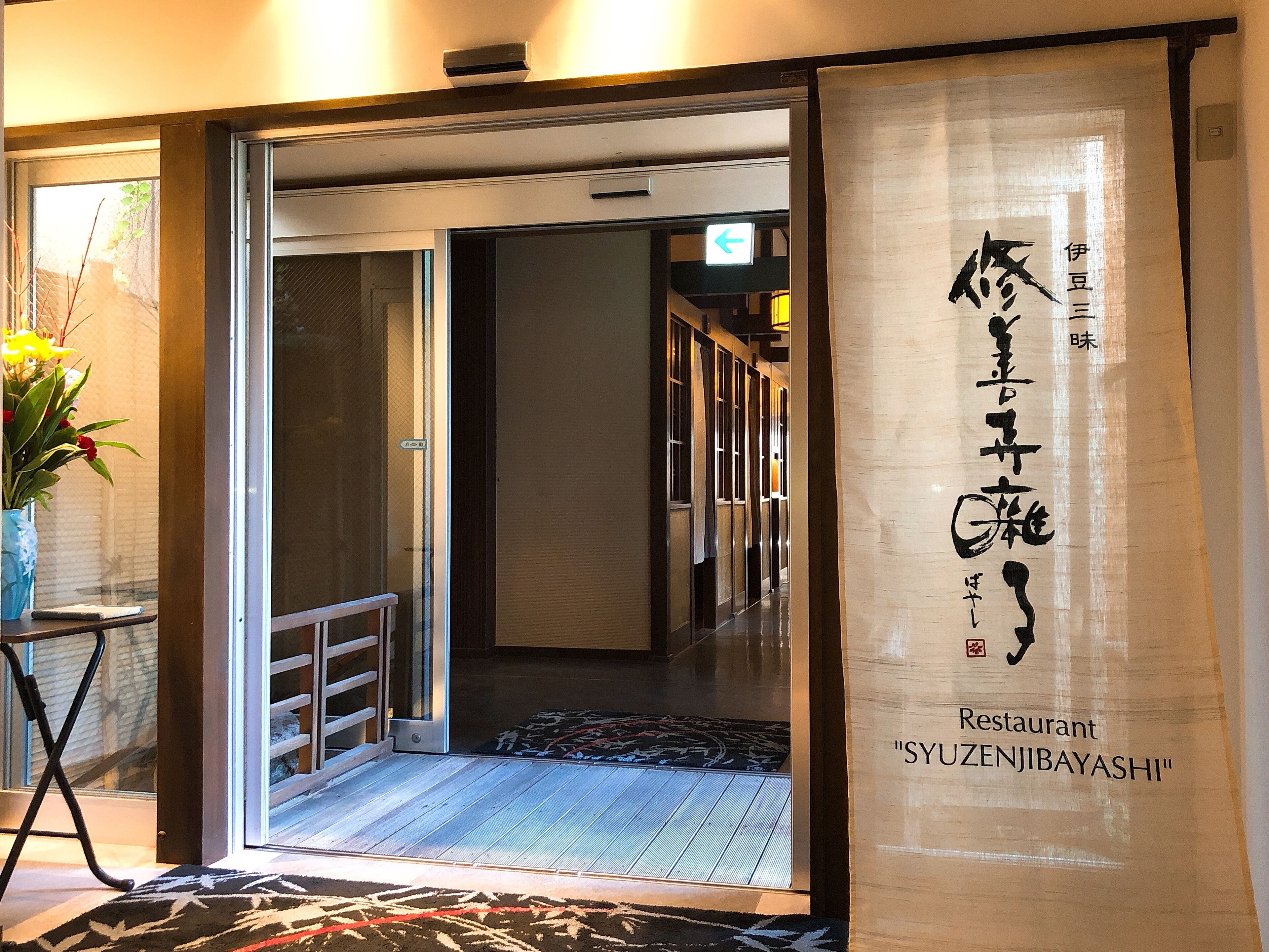 A traditional Japanese restaurant entrance with a sliding door, a wooden floor, and a patterned rug.