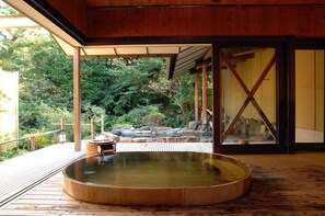 A wooden deck with a hot spring bath, surrounded by a wooden pergola and a view of a garden with rocks and trees. - Yukairou Kikuya (Izu)