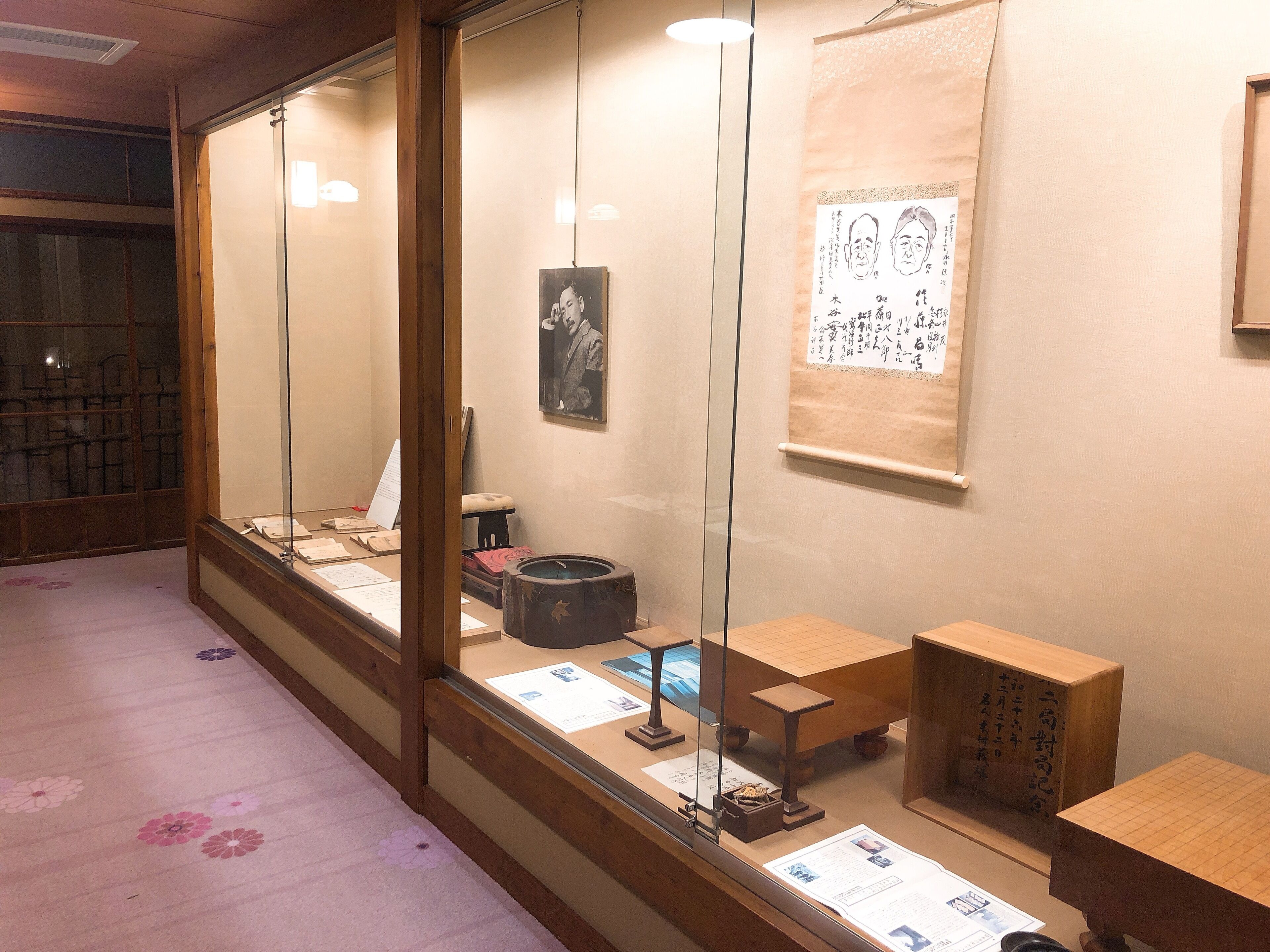 A room with a traditional Japanese aesthetic, featuring tatami flooring, a low wooden desk, and a display case with cultural artifacts.
