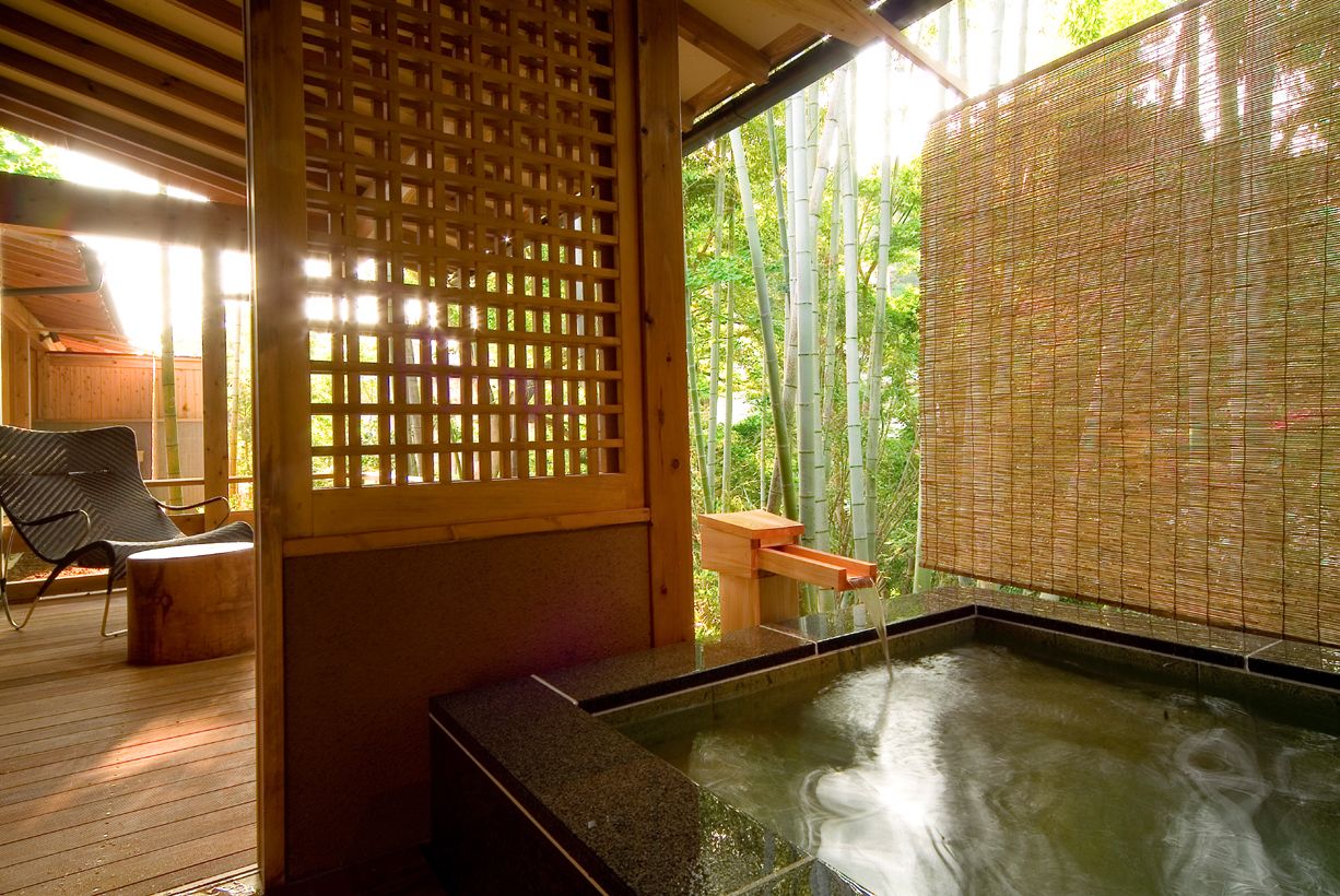 Un onsen japonés tradicional con una terraza de madera, un fondo de bambú y vistas a árboles de bambú.