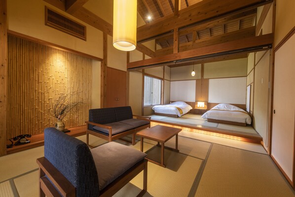 A traditional Japanese-style room with tatami flooring, a low wooden bed, a sofa, and a small table. - Yukairou Kikuya (Izu)