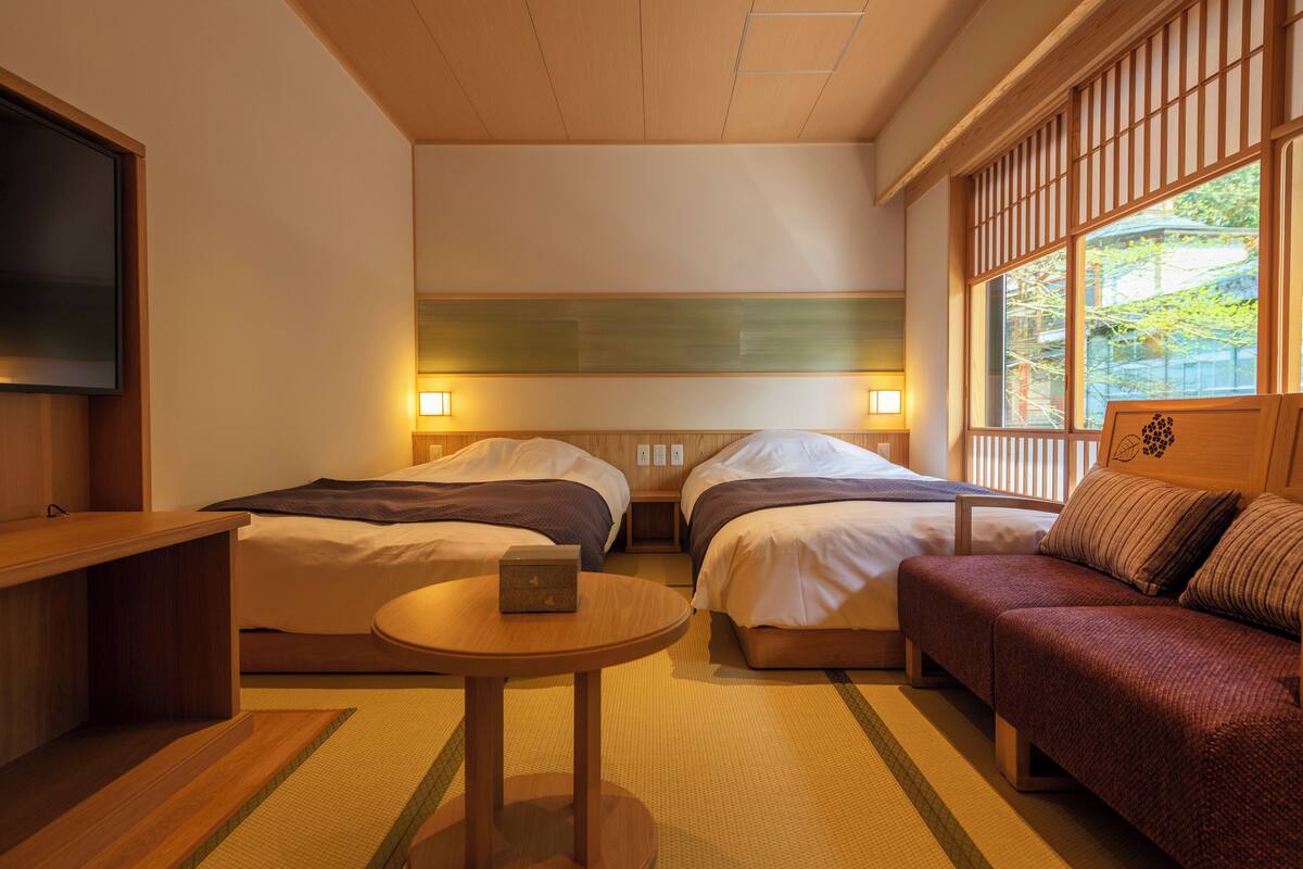 Ein Hotelzimmer mit zwei Betten, einem Sofa, einem Fernseher und einem kleinen Tisch.