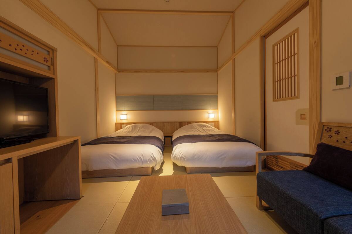 Ein Hotelzimmer mit zwei Betten, einem Fernseher, Nachttischlampen, einem Holztisch und einem Sofa.