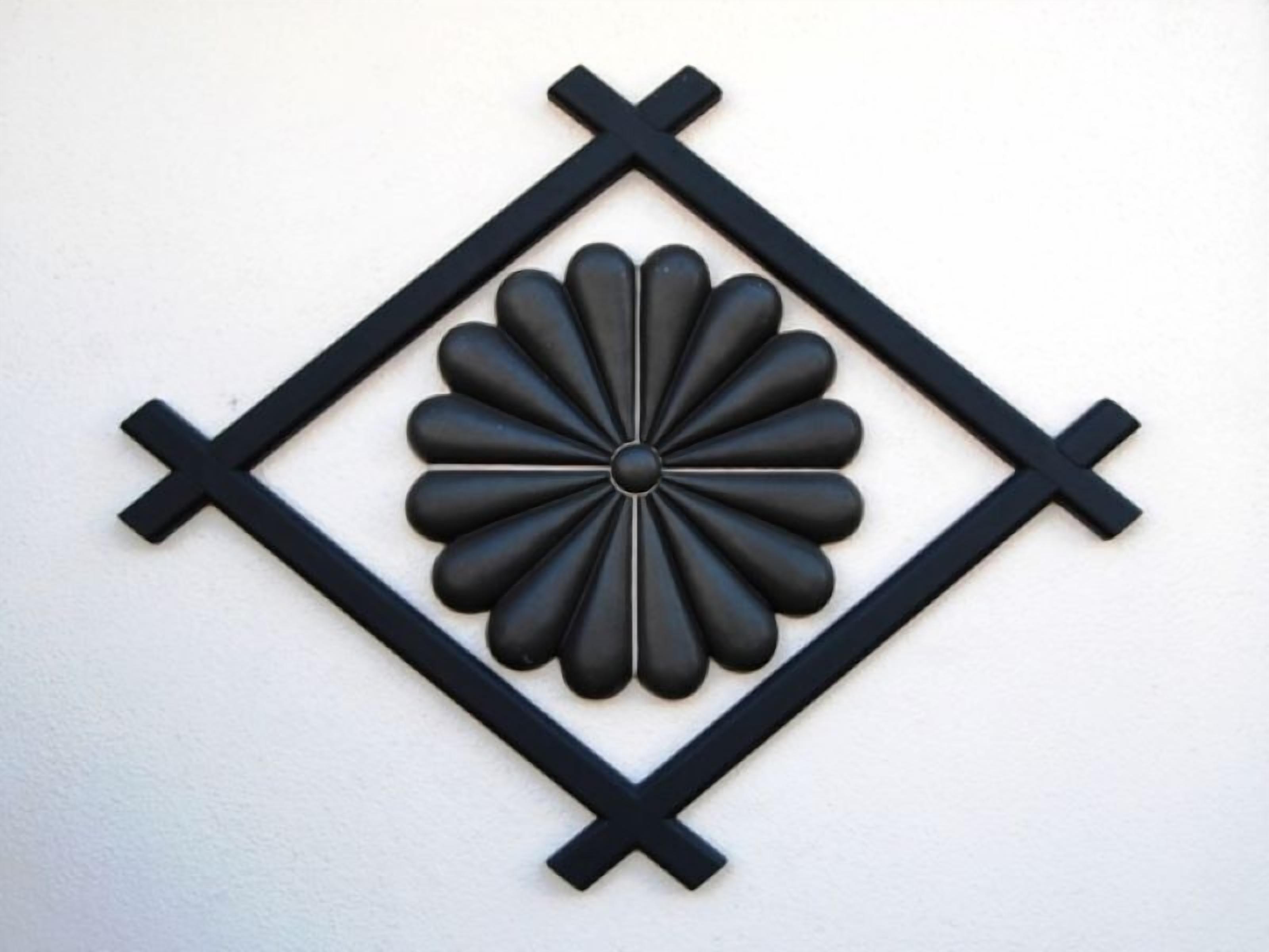 A black decorative wall piece with a central floral design surrounded by a diamond pattern.