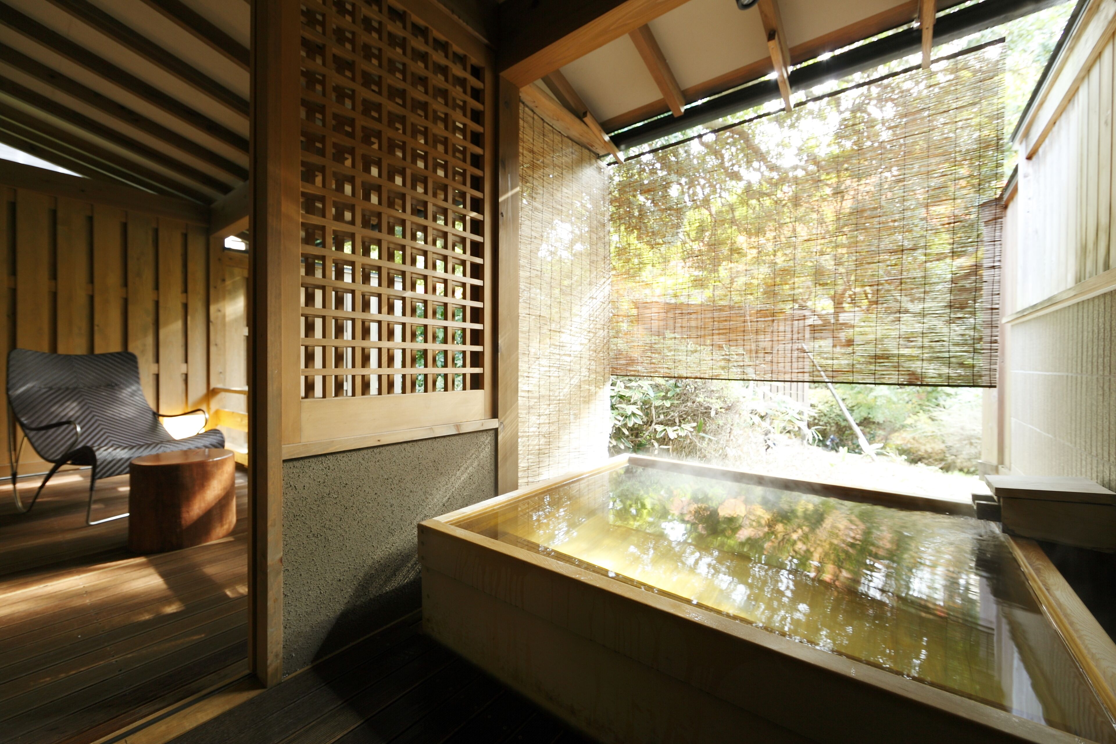 A traditional Japanese room with tatami flooring, a wooden bench, a large wooden bathtub, and a view through a shoji screen.