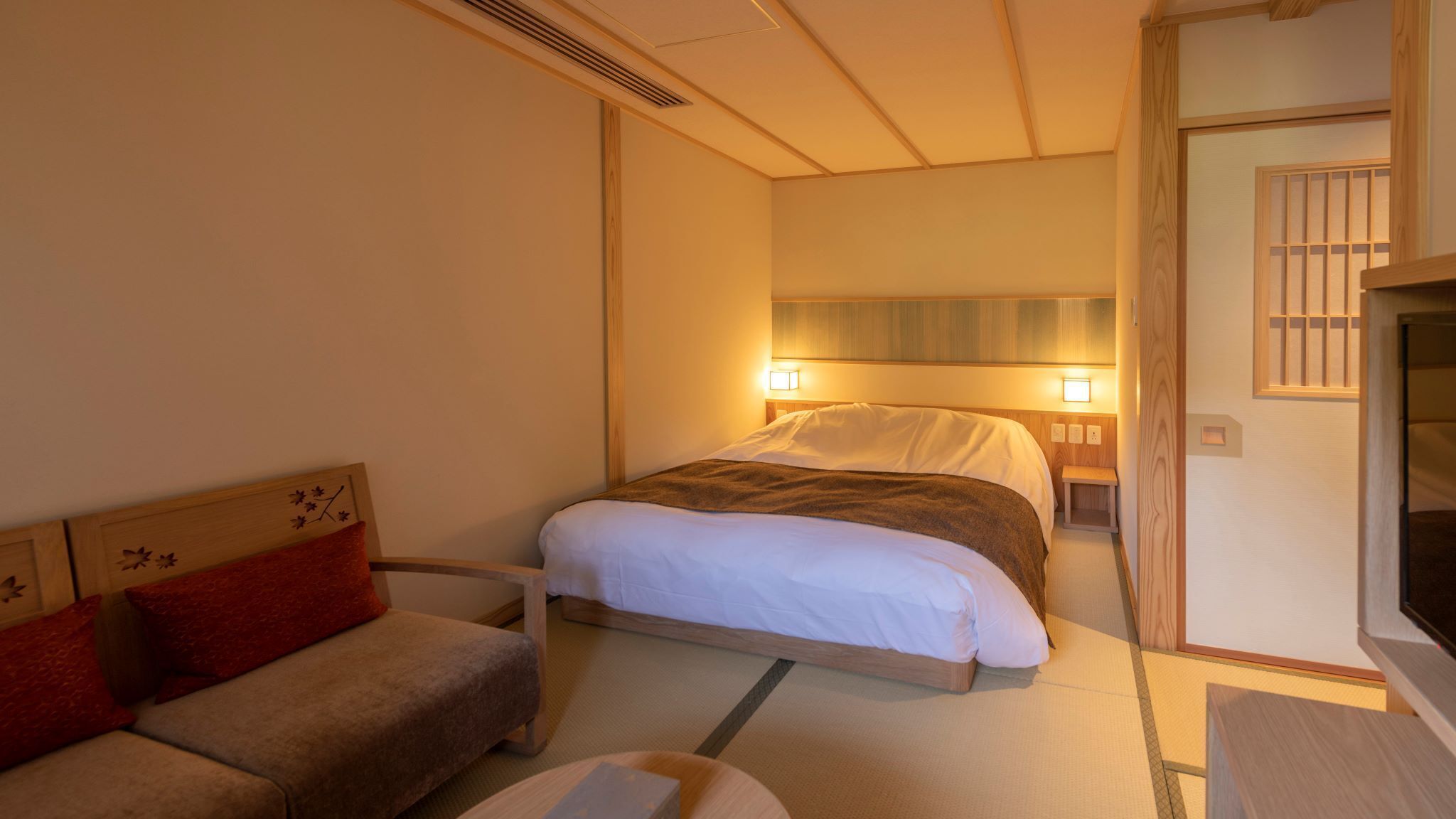 A hotel room with a bed, a sofa, a TV, and a small wooden table.