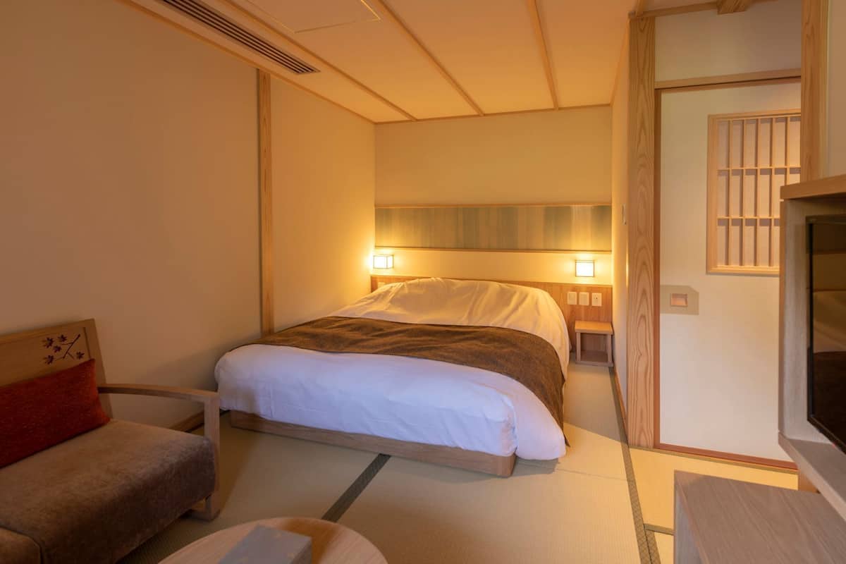 Habitación de hotel con cama, sofá, televisor y una pequeña mesa de madera.