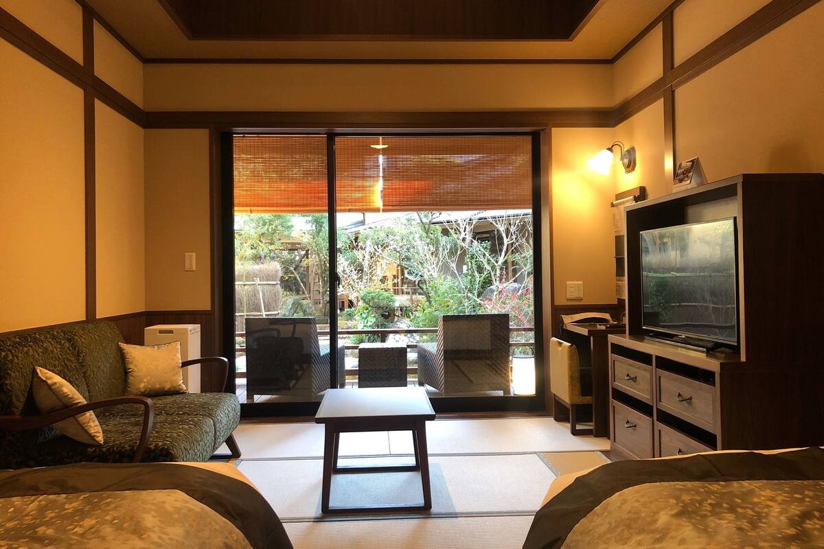Ein traditioneller japanischer Raum mit Tatami-Boden, einem niedrigen Tisch, einer Couch und einem Fernseher.