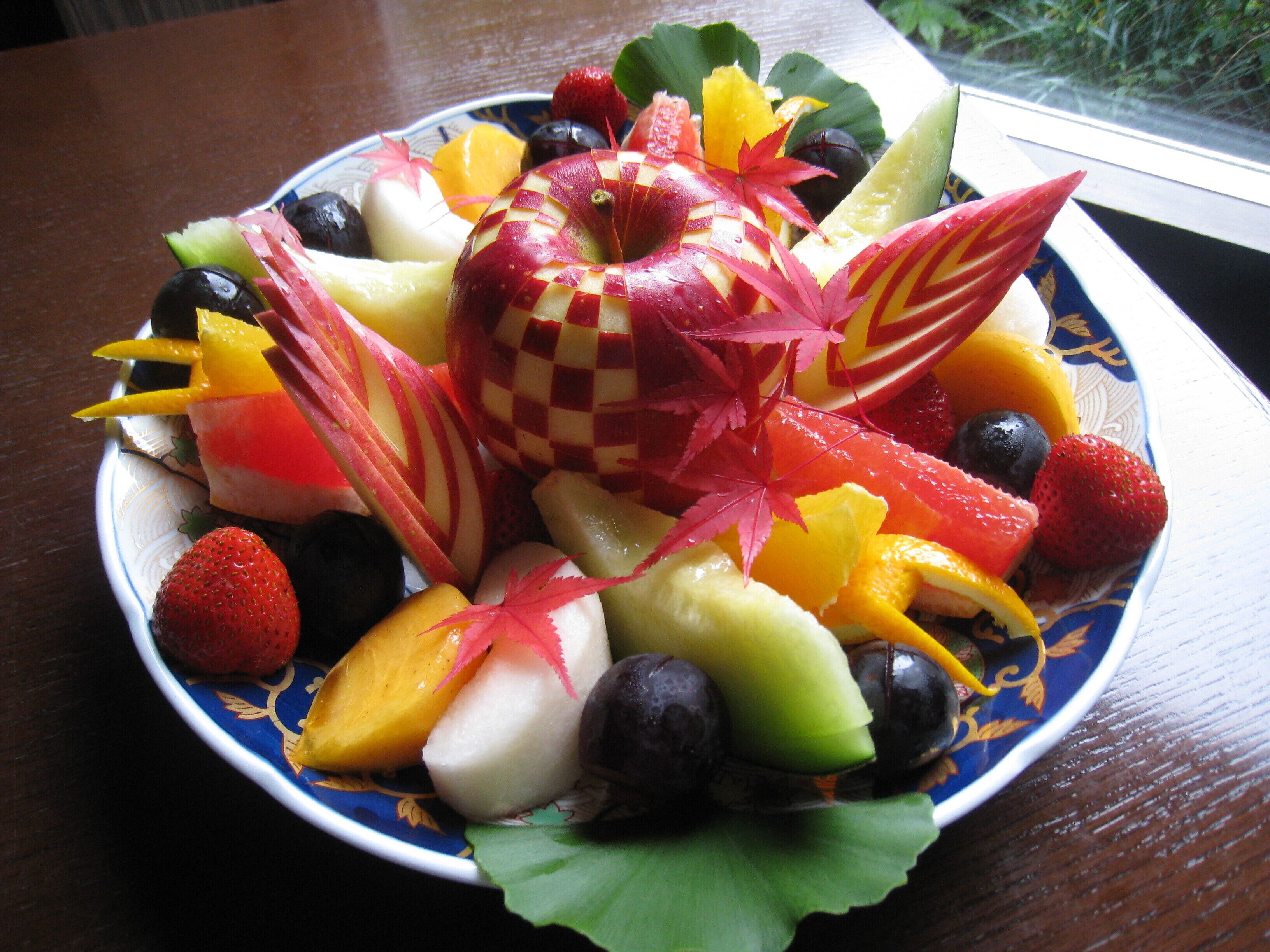 A fruit platter with various fruits and a decorative leaf on a plate.
