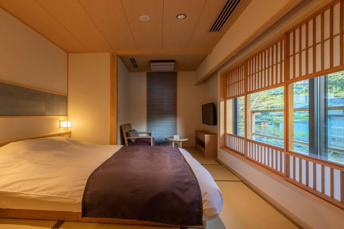 Ein Hotelzimmer mit Bett, Nachttisch, Sessel, Fernseher und großen Fenstern mit Blick.